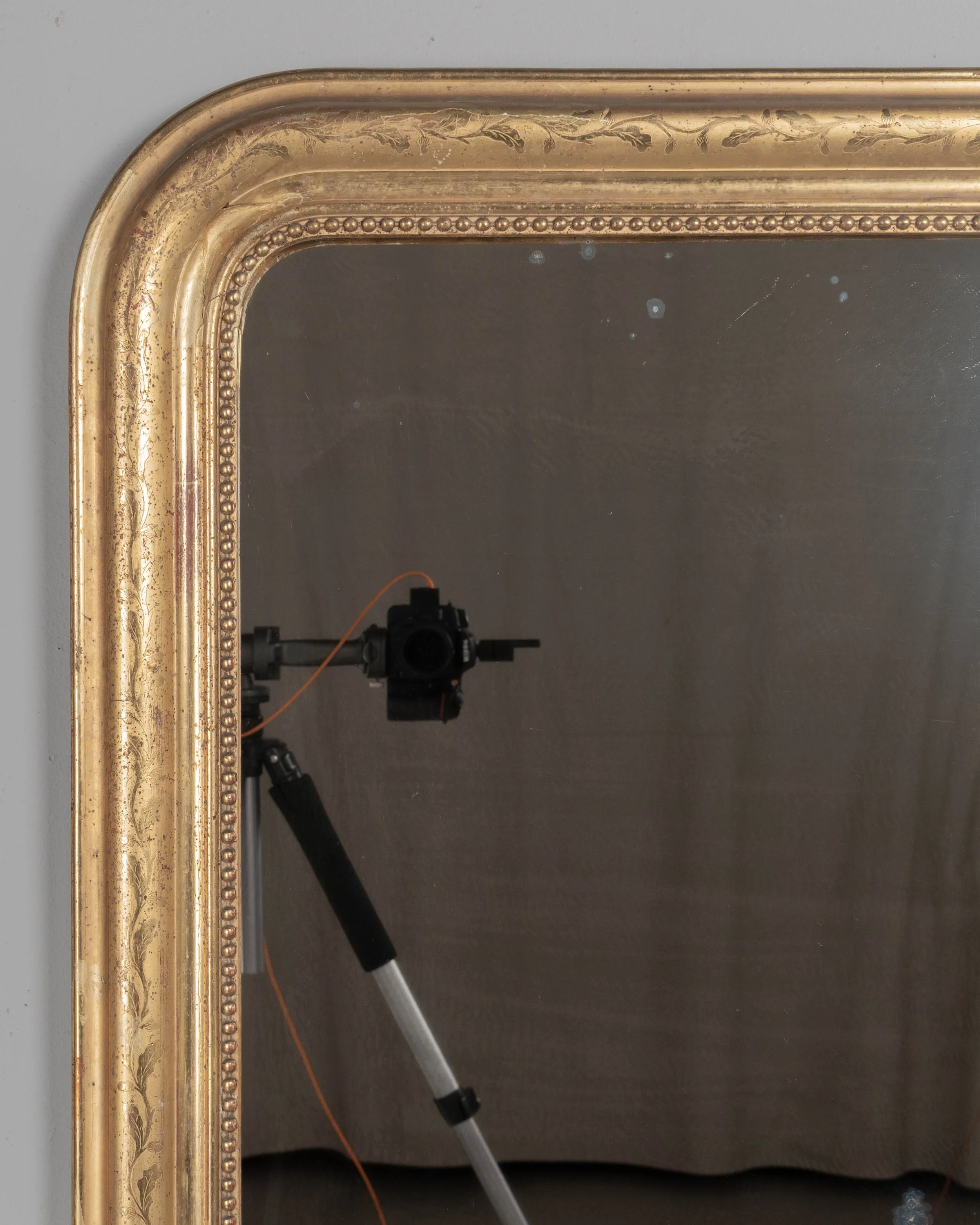 SAn early 20th century French Louis Philippe style gilded mirror with curved top corners, incised floral decoration and inner bead border.