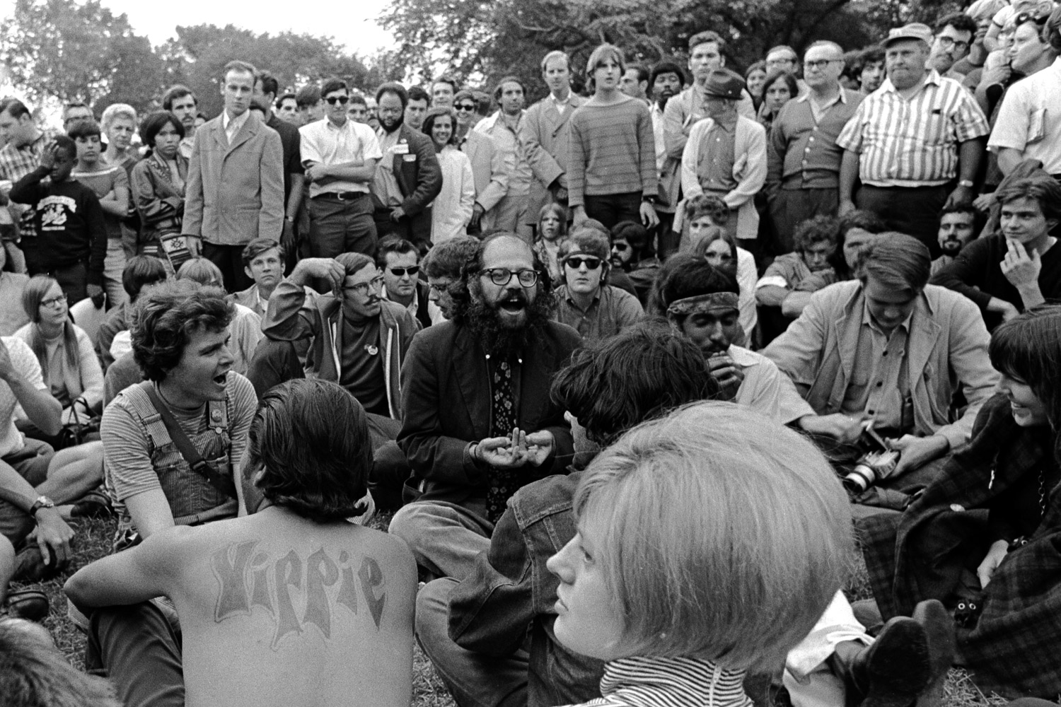  Allen Ginsberg is chanting "om" in long, sustained breaths, joined by hundreds of participants from all walks of life. 