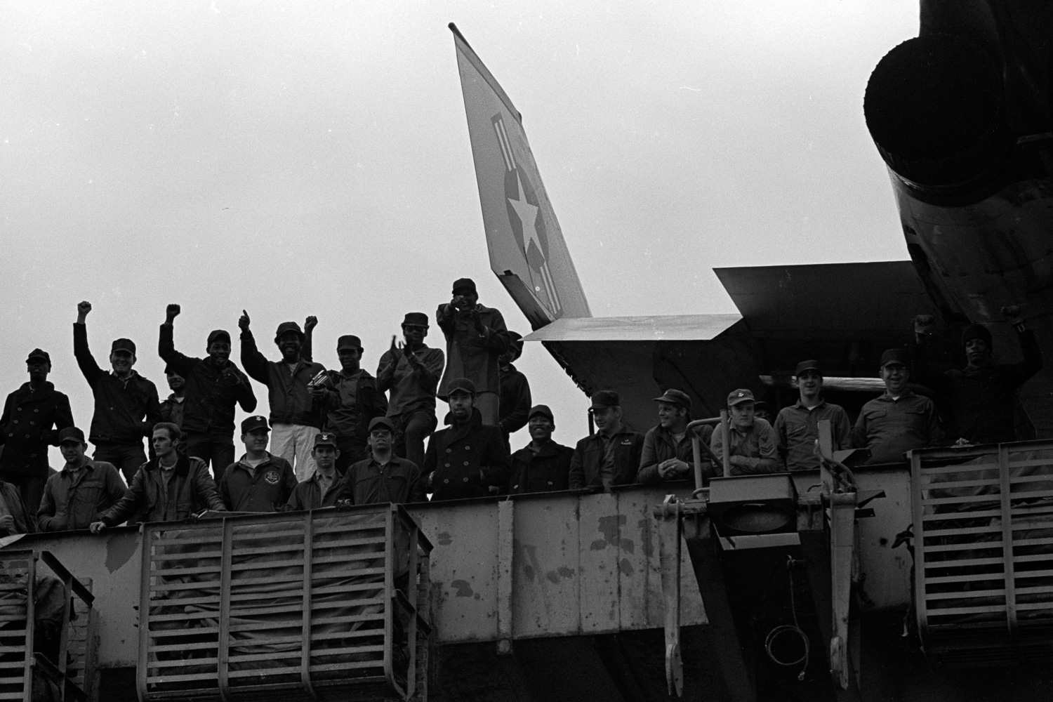  Crewmen on the deck of the USS Coral Sea respond with cheers when Navy wives on shore display their banner. 