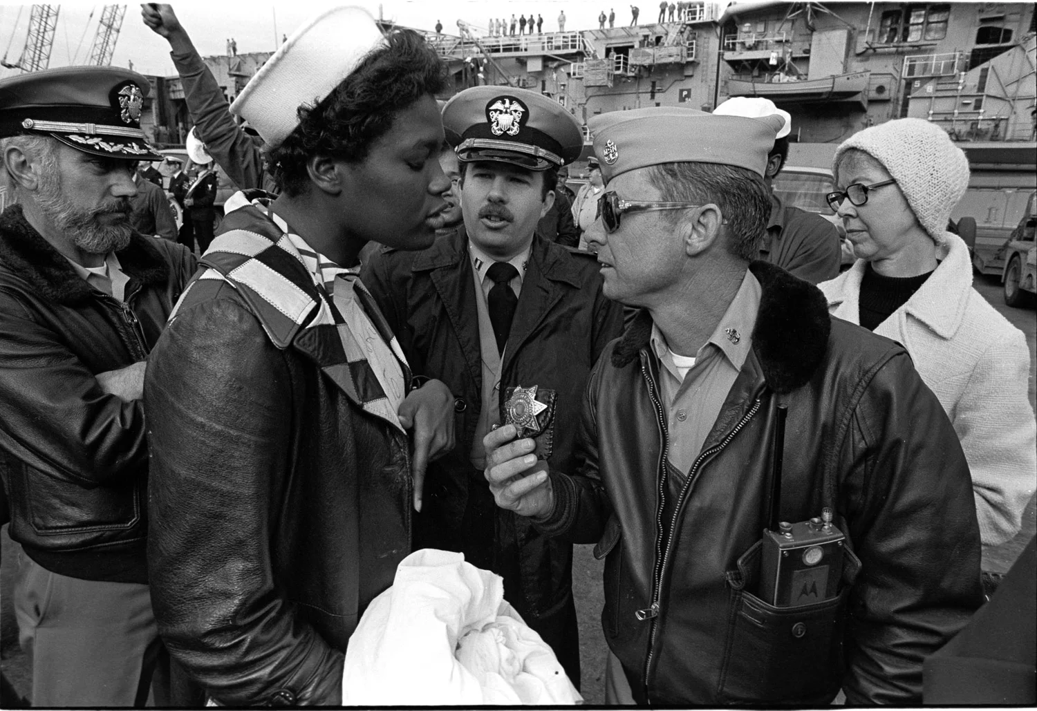 Rose Hills, Navy wife (left), squares off to base security at NAS Alameda, refusing to surrender the banner in her hands. It reads "Good luck on your captain's suicide mission."