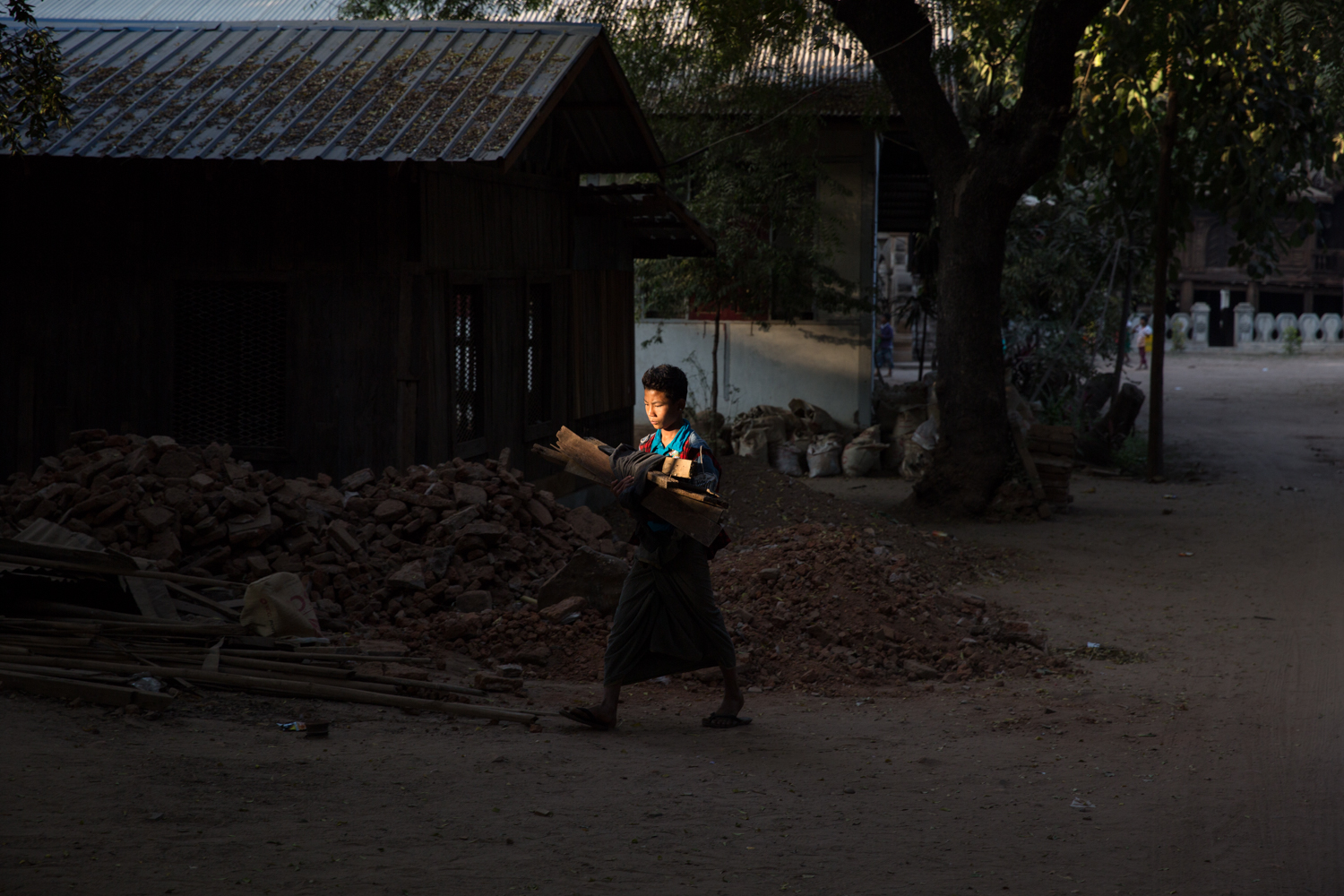 A boy carries firewood through a lonely sliver of light back to his home in Bagan, Myanmar.