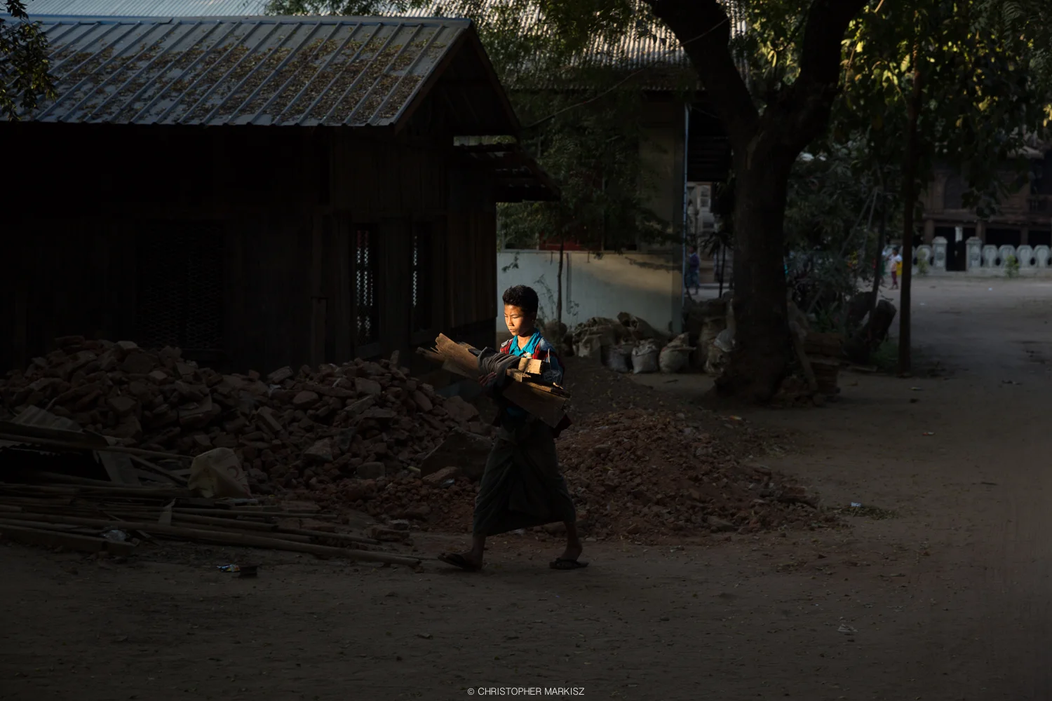 A boy carries firewood through a lonely sliver of light back to his home in Bagan, Myanmar.