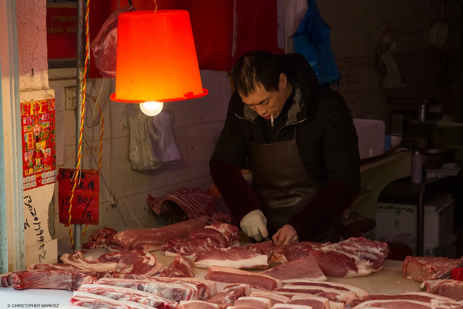 A butcher smokes a cigarette while preparing cuts of meat for sale at a market in Shanghai, China.