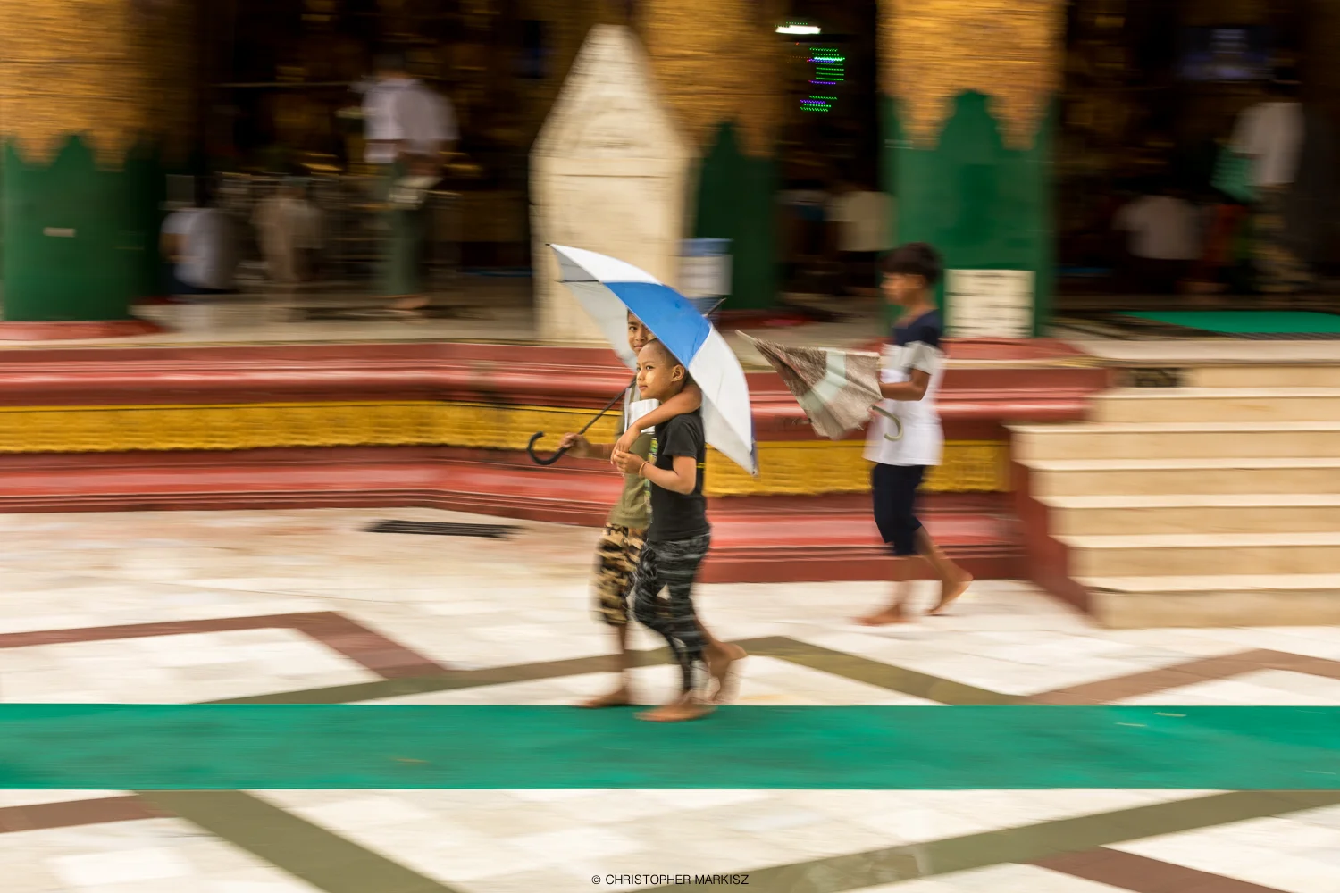 Children walking under an umbrella on a rainy day at Shwedagon Pagoda in Yangon, Myanmar.
