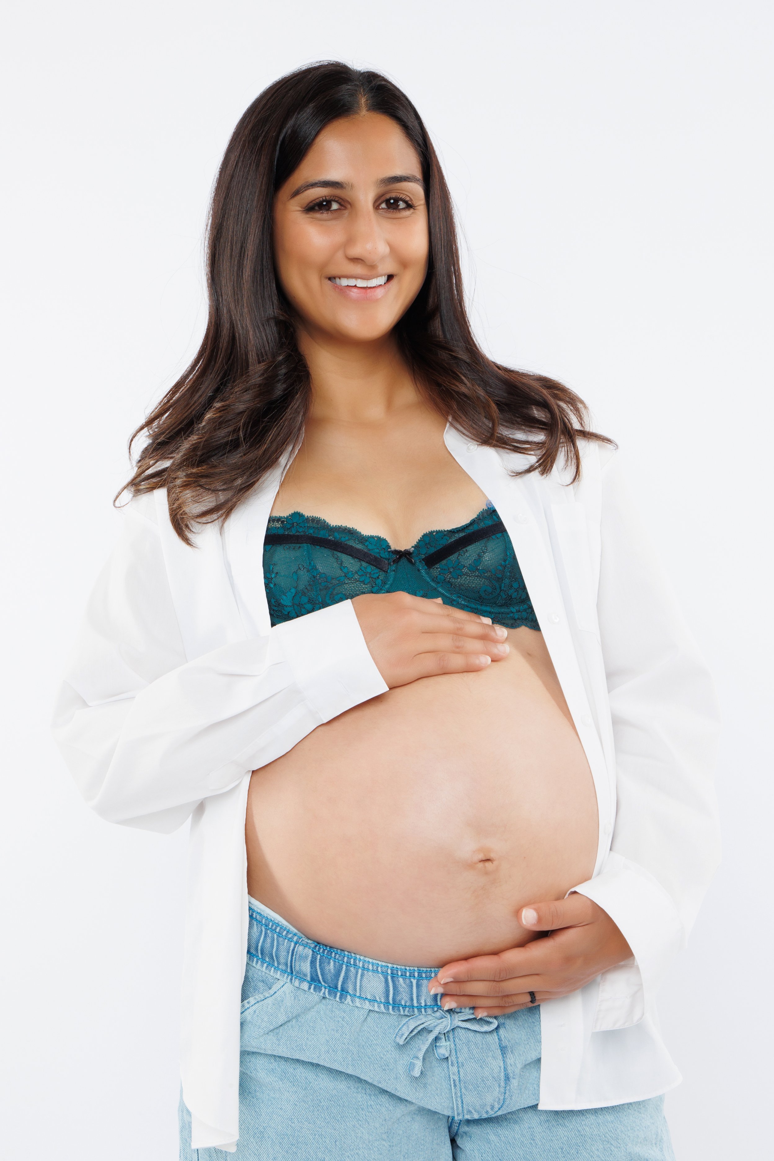 Maternity portrait in an open white shirt and jeans against a light background.