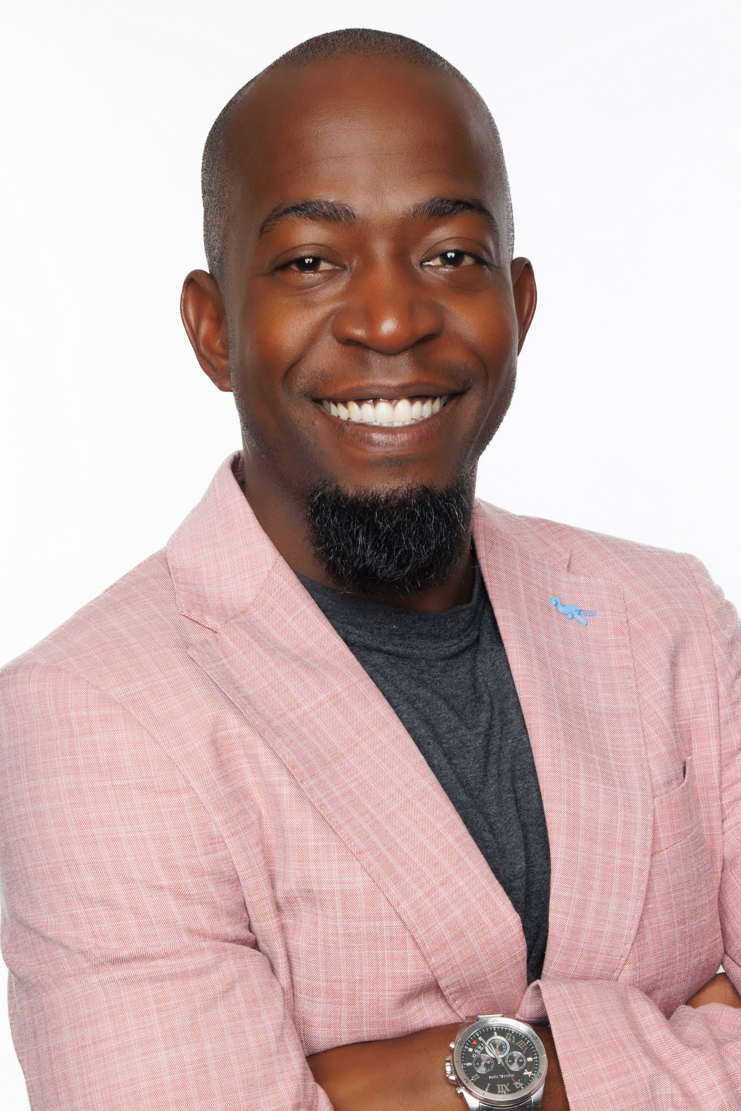 Smiling professional headshot of a man in a pink blazer against a white background.