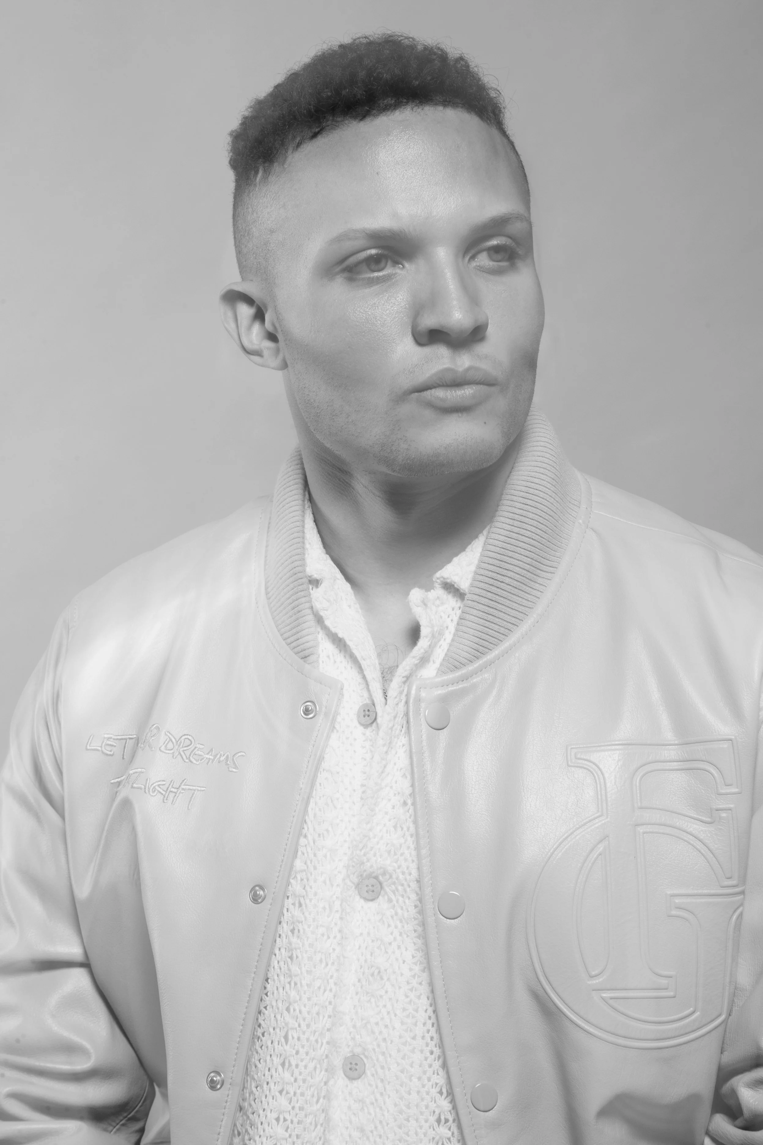 Black-and-white studio portrait of a man in a light varsity jacket looking to the side.