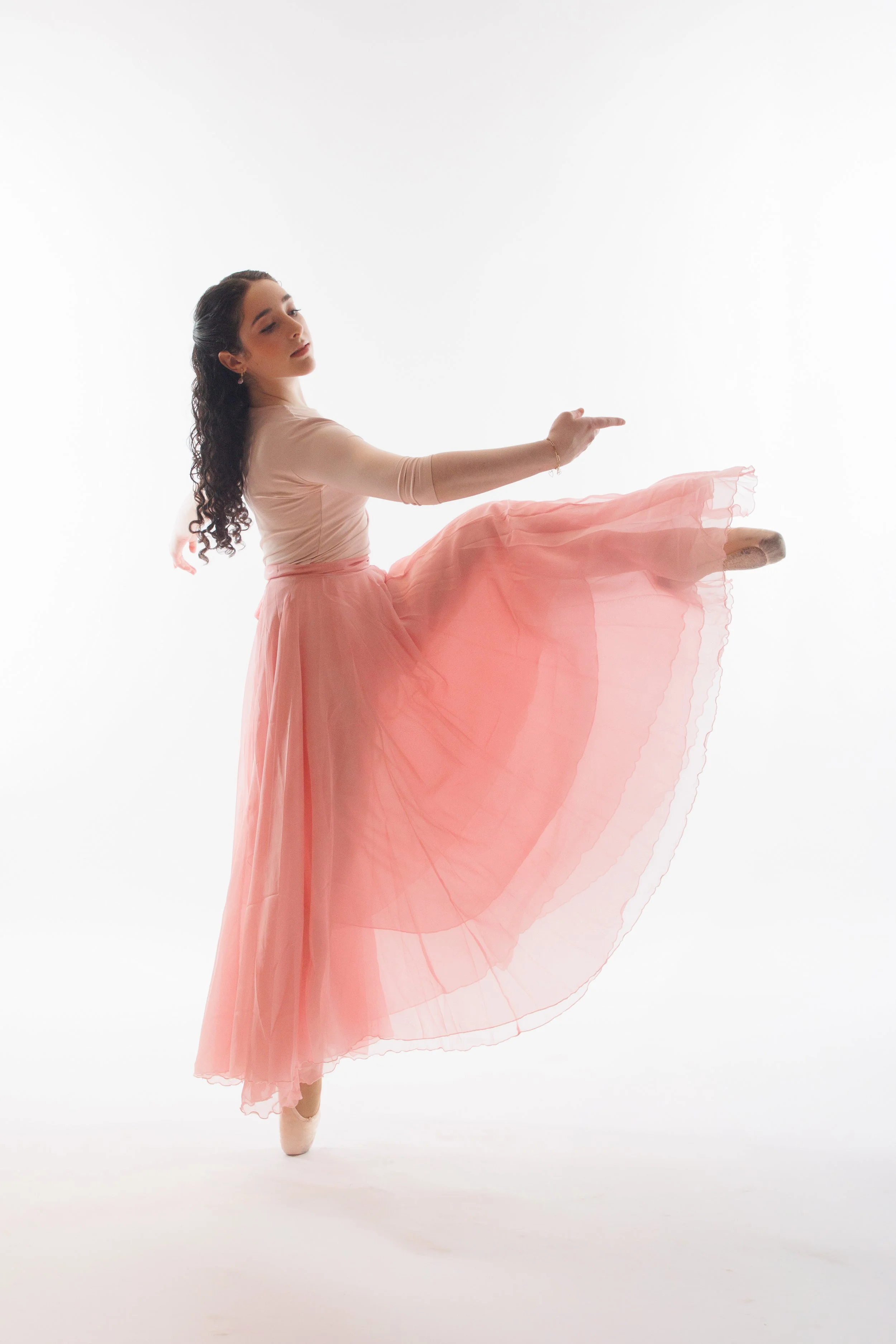 Full-length ballet portrait of a dancer en pointe with one leg extended in a pink skirt.