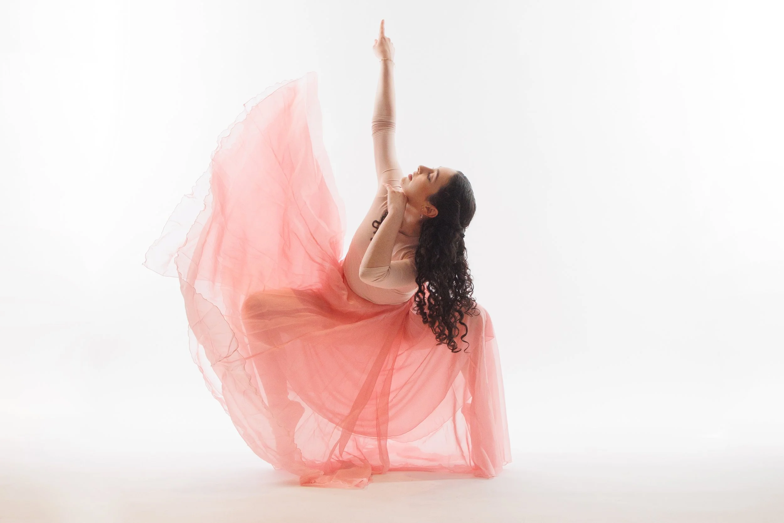Dancer bending sideways with an arm raised and a flowing pink skirt sweeping upward.