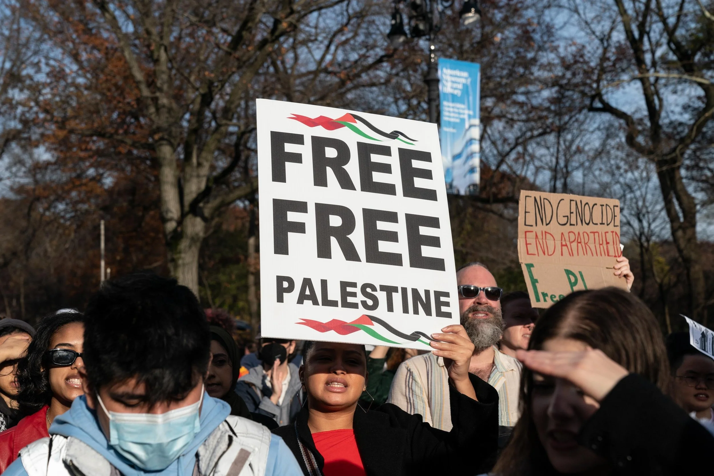 A demonstrator holds a “Free Free Palestine” sign among a crowd at a public rally.