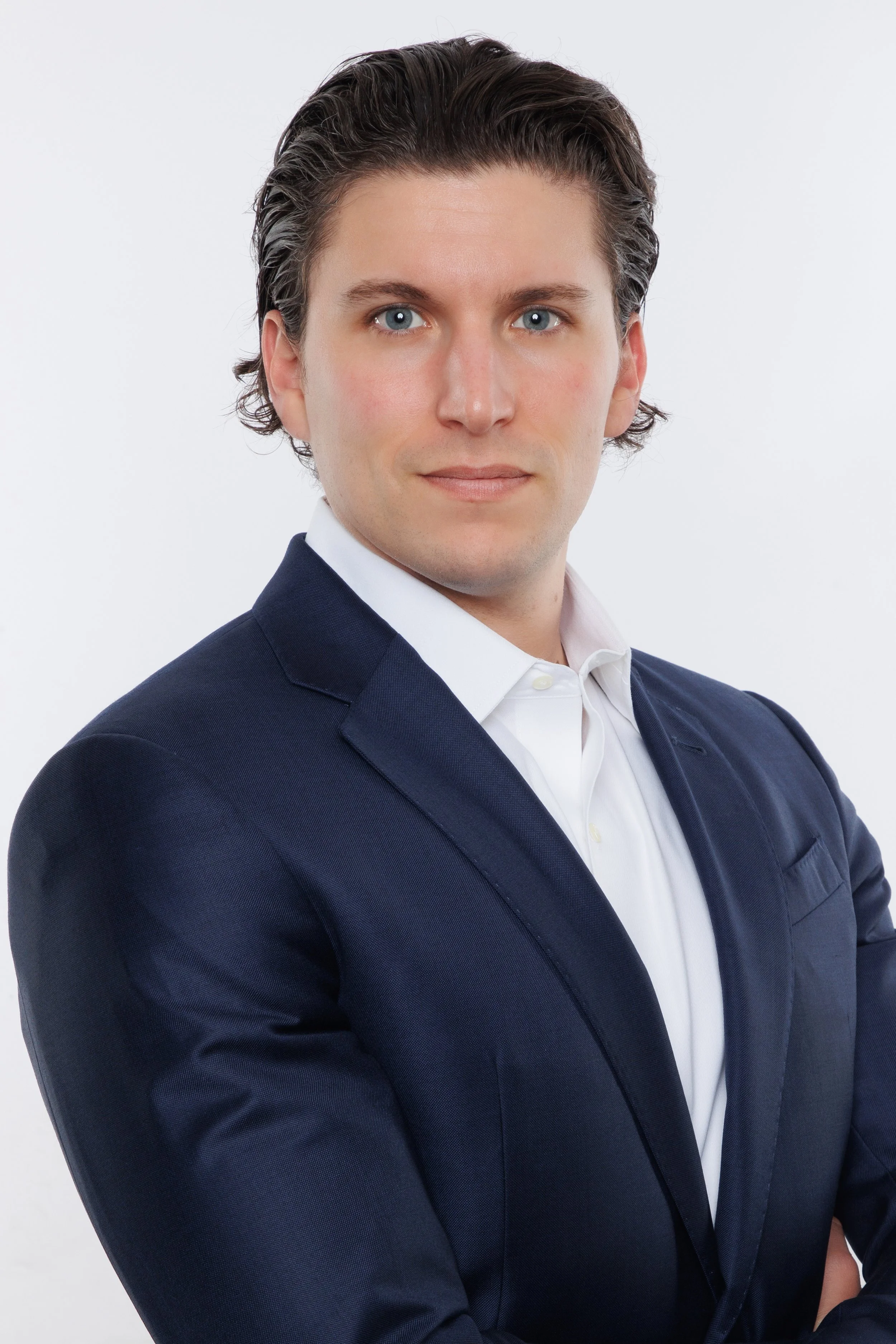 Professional studio headshot of a man in a navy suit and white shirt against a light background.