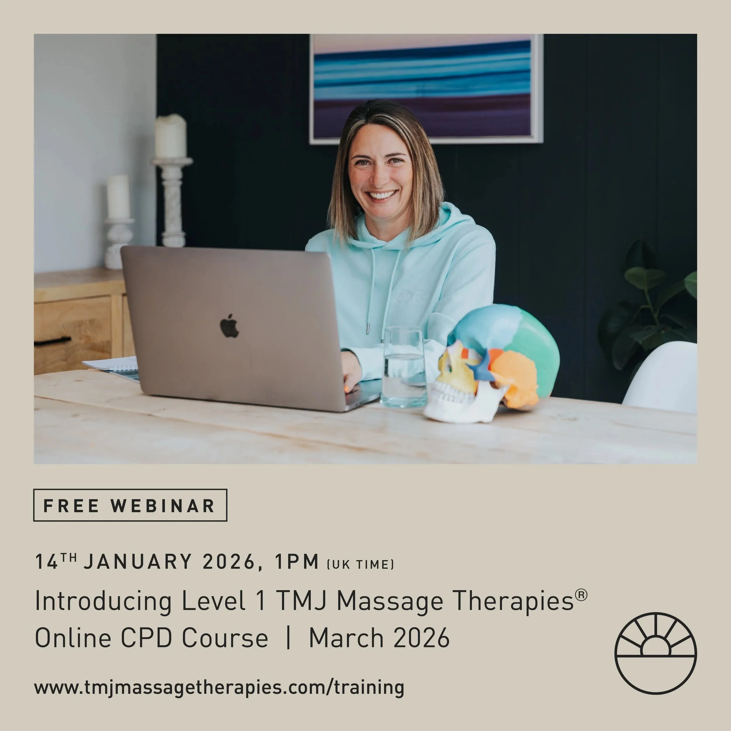 A woman with shoulder-length hair sitting at a wooden table with a laptop, a glass of water, and a colorful skull model, in a modern room with a black wall, a framed artwork, and candles.