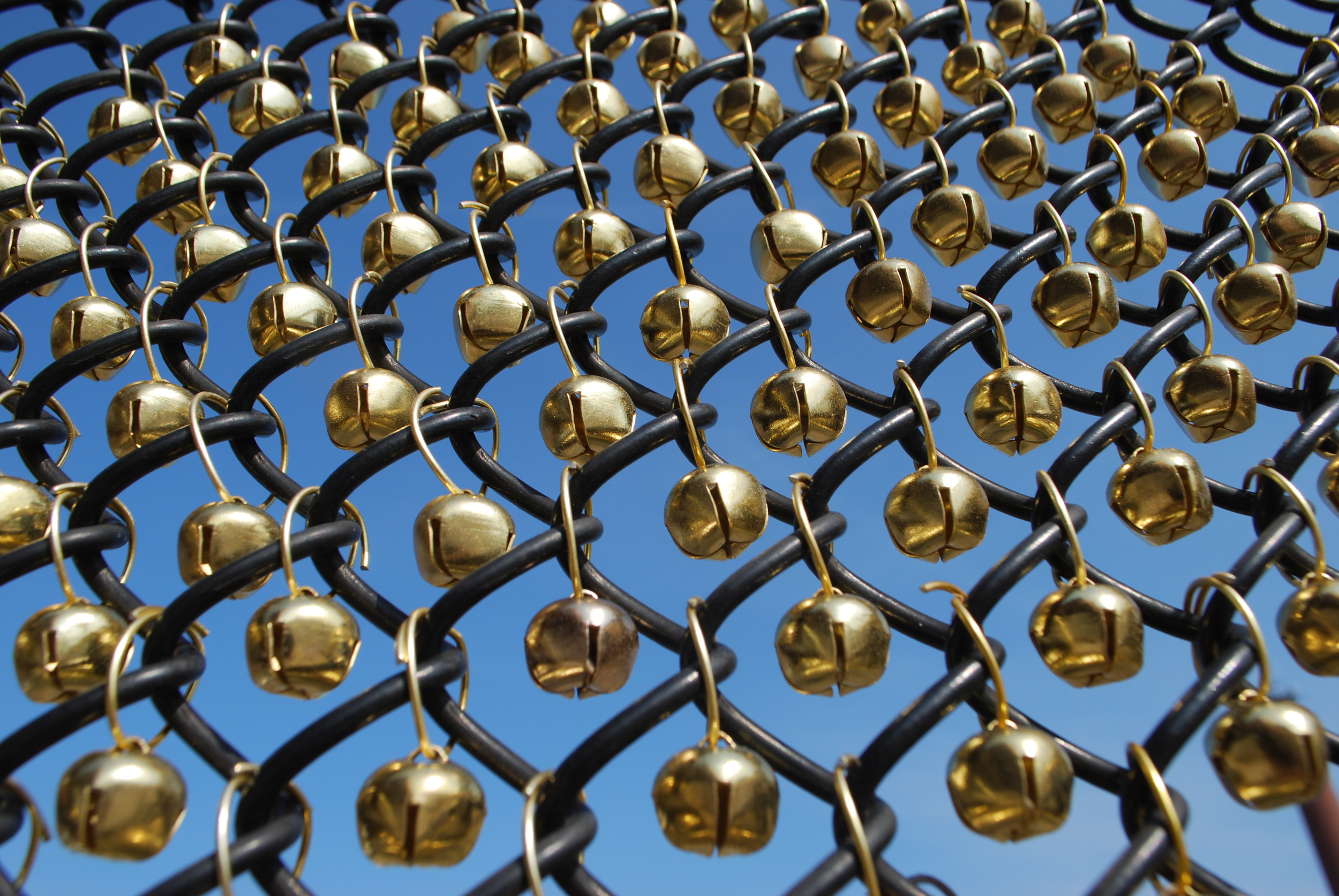 Each bell hung from a single jump in the opening of a chain link fence.