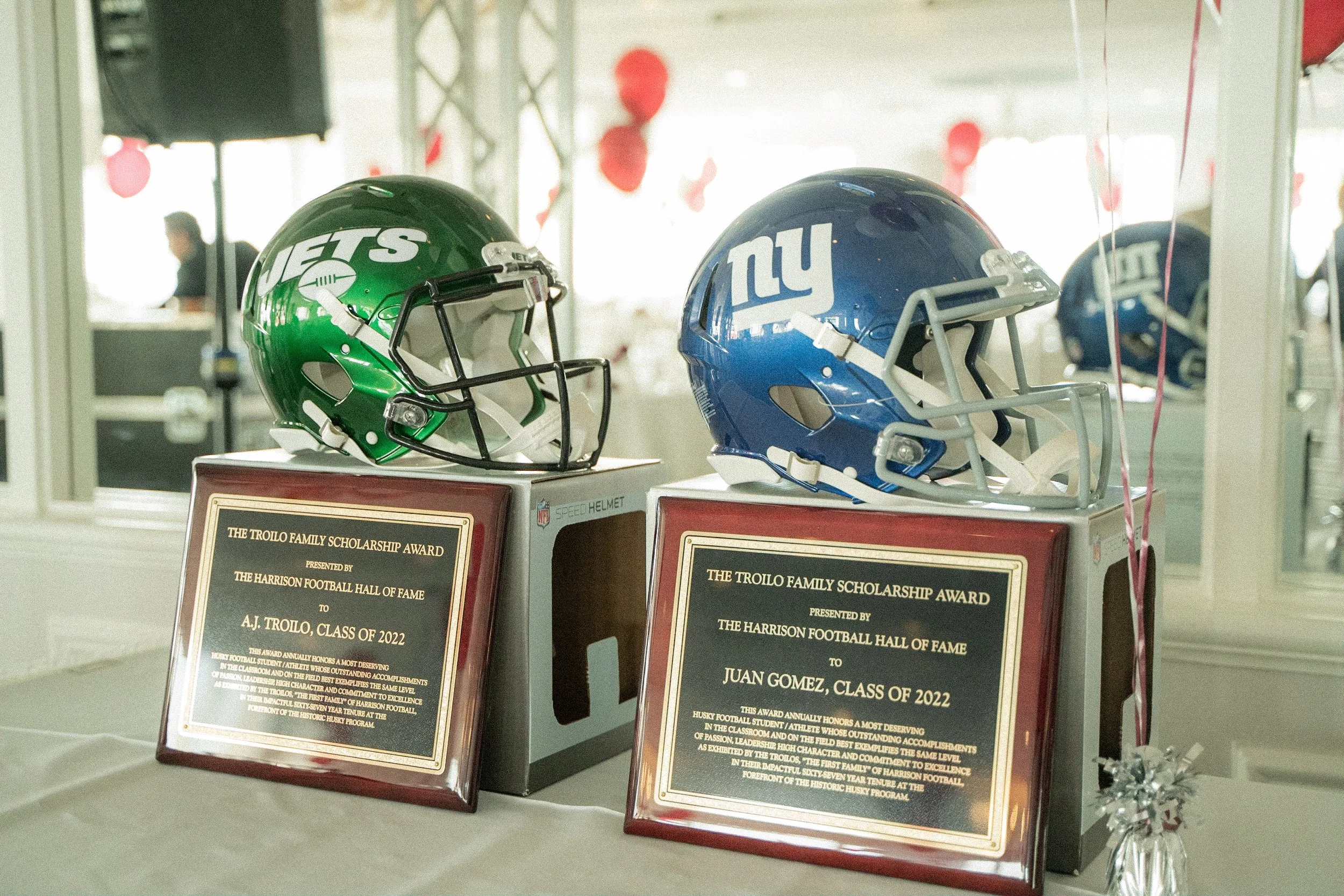 Two football helmets, one green with the New York Jets logo and one blue with the New York Giants logo, displayed on award plaques at a ceremony.