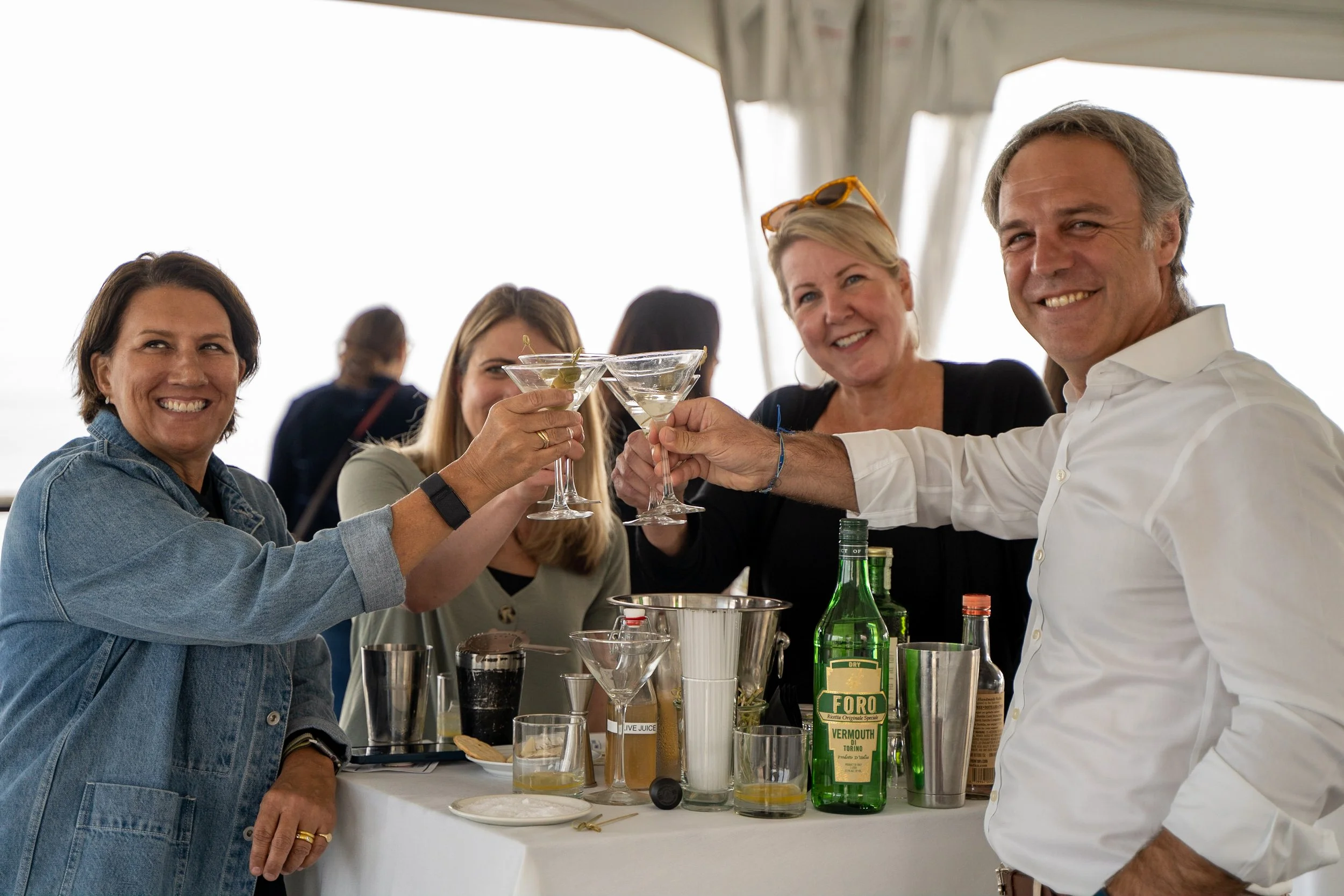 Smiling group of four people raising cocktail glasses in a toast at a social gathering on a boat or outdoor venue.