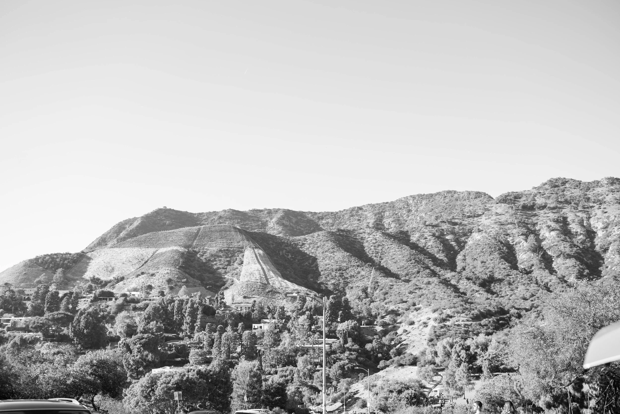 Black and white photo of a mountainous landscape with scattered houses and trees at the base of the hills.