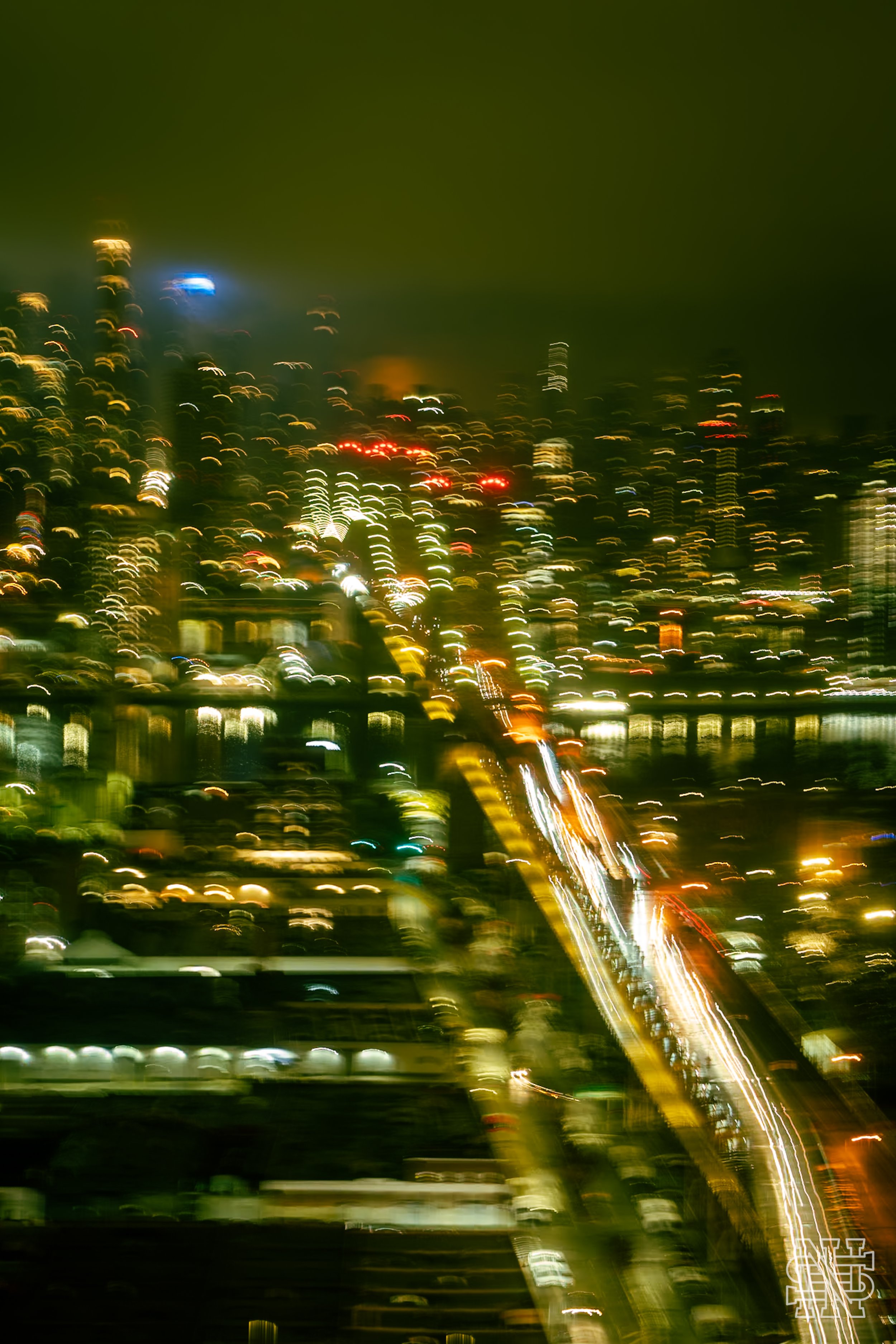 A blurred nighttime cityscape with bright lights and a road with moving vehicles.