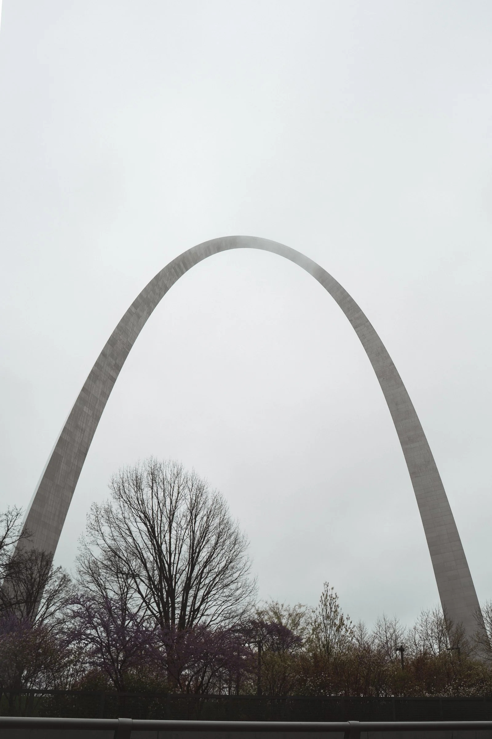 The Gateway Arch in St. Louis, Missouri, seen from below, with leafless trees and a cloudy sky.