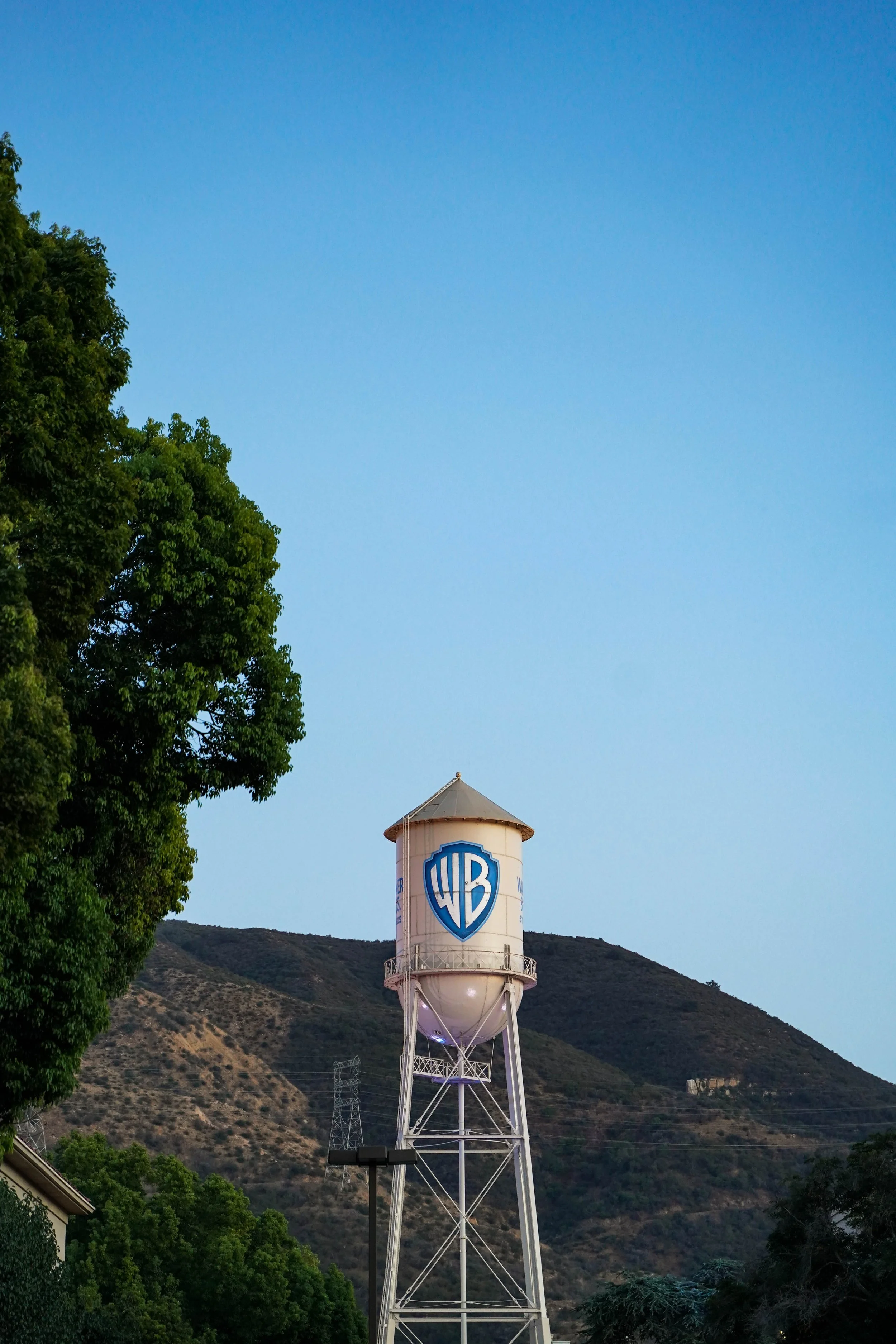 A water tower with the Warner Bros. shield logo against a backdrop of mountains and a clear blue sky.