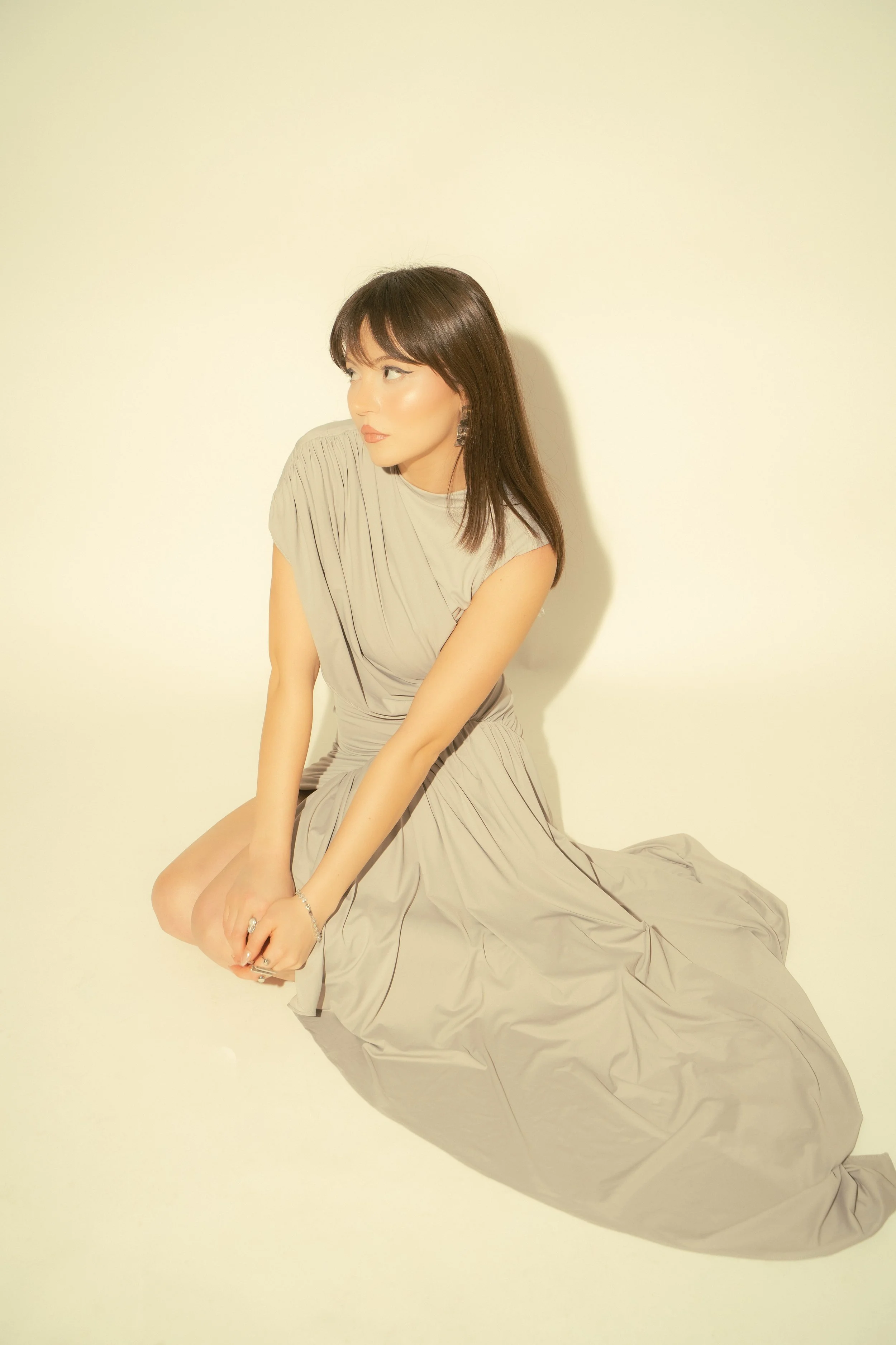 Woman in a beige dress sitting against an off-white background.