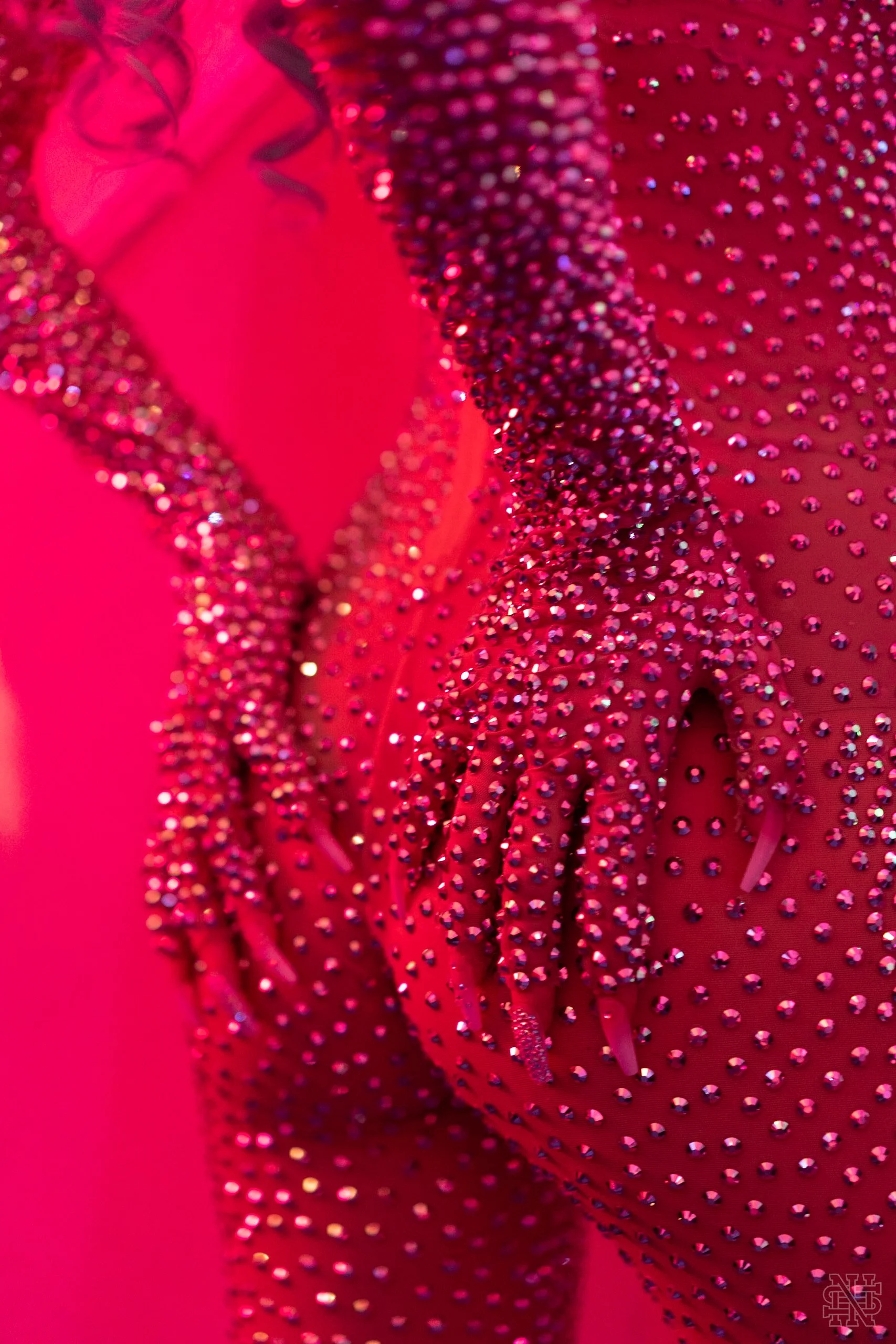 Close-up of a figure skating costume embellished with pink rhinestones, with the figure's hand resting on their chest.