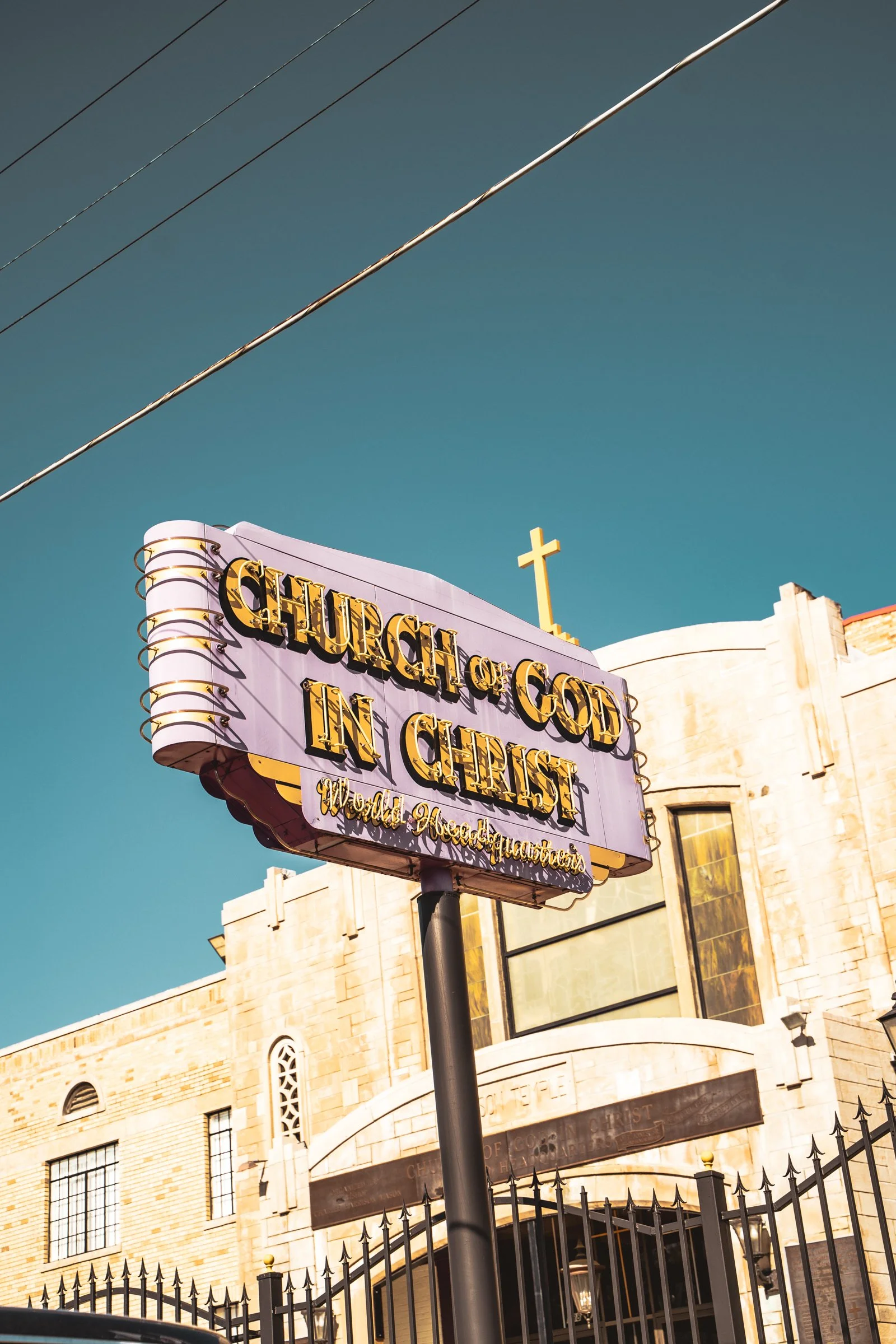 A church sign reads 'Church of God in Christ' with a purple background and gold lettering, with a church building and cross in the background.