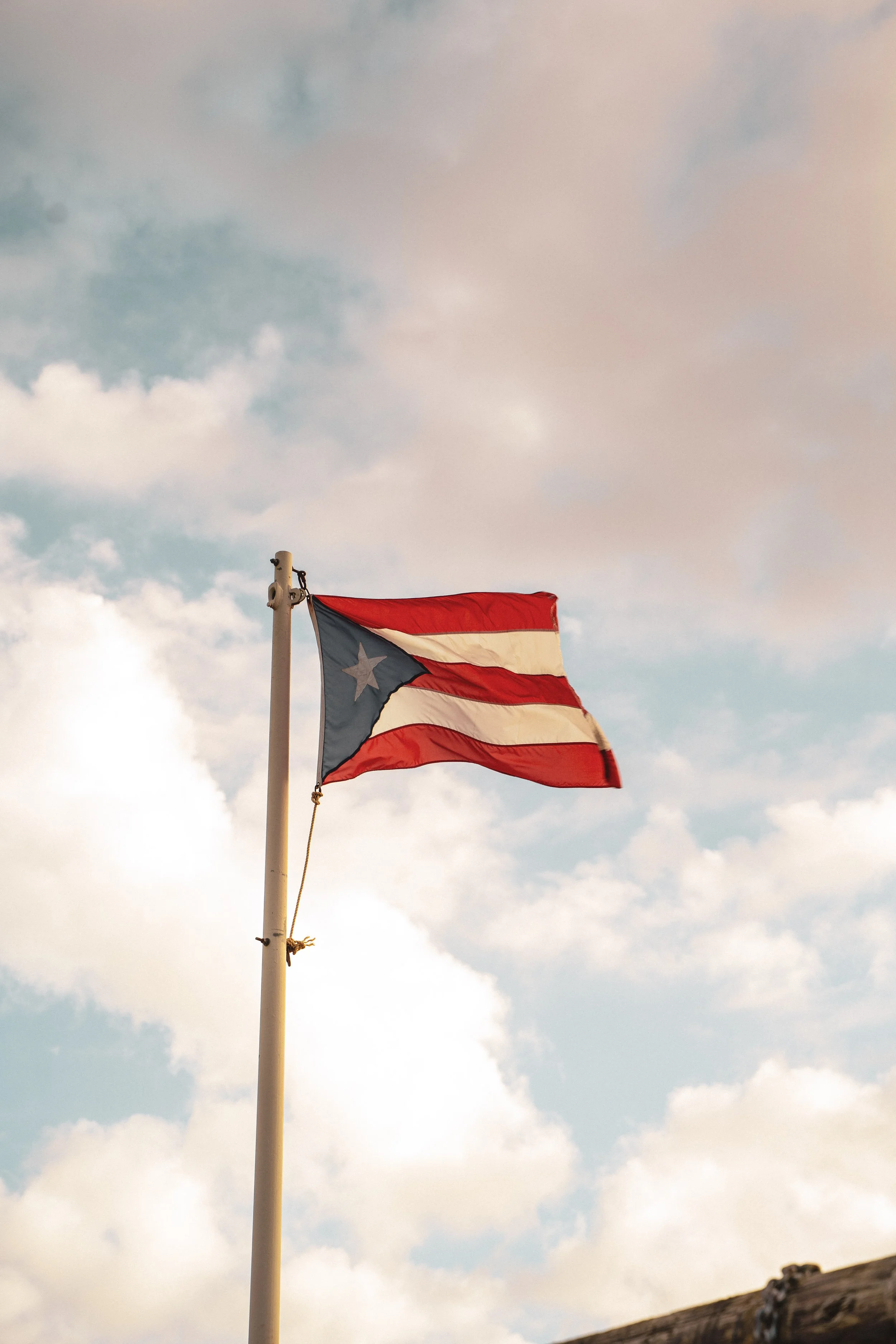 Puerto Rican flag flying on a flagpole against a cloudy sky.