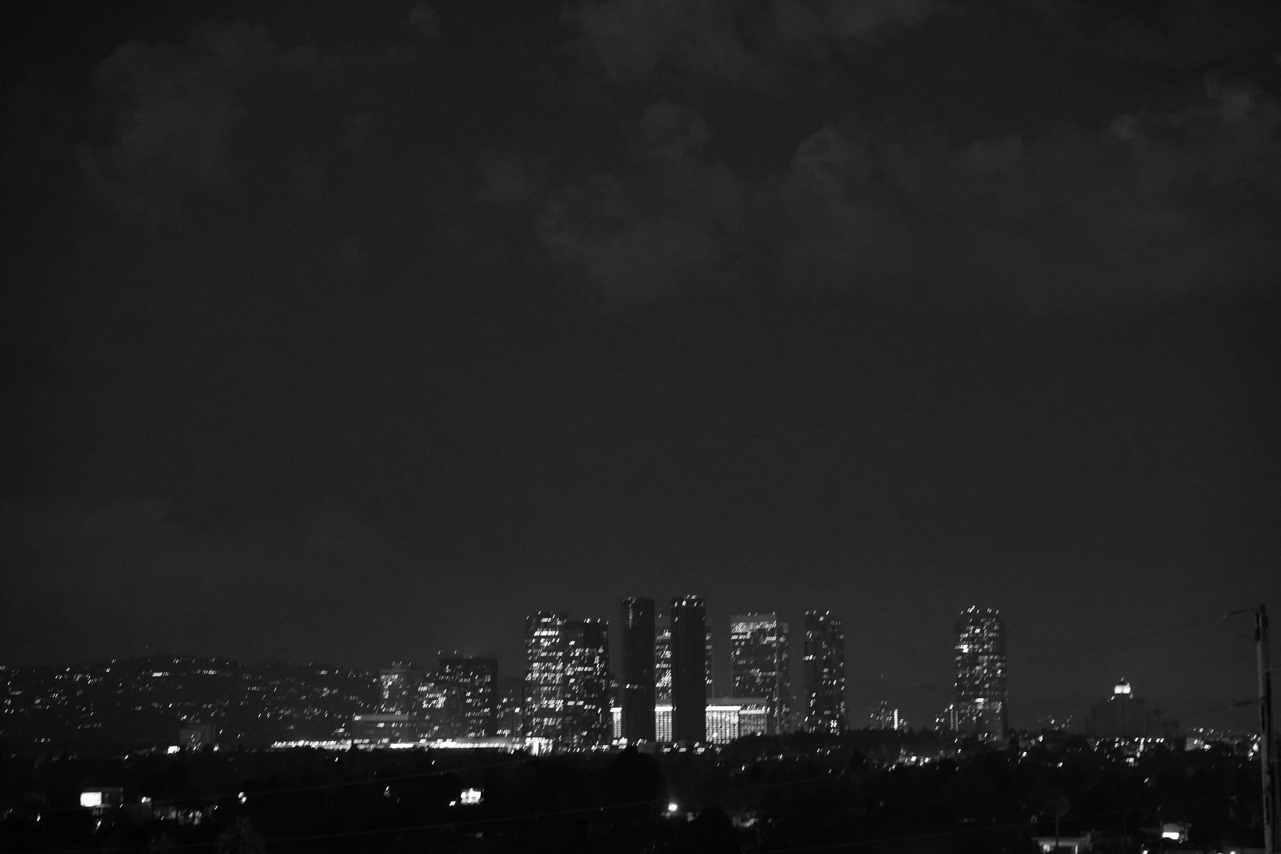 Nighttime cityscape with illuminated high-rise buildings and dark sky with clouds