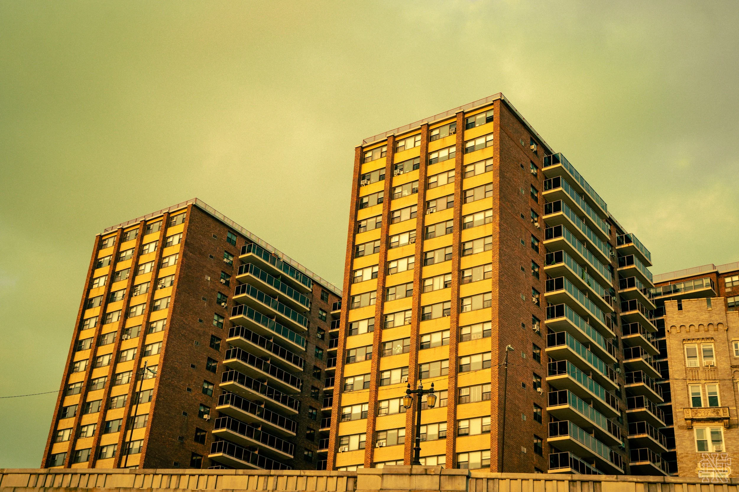 Three tall apartment buildings with numerous balconies against a yellowish sky.