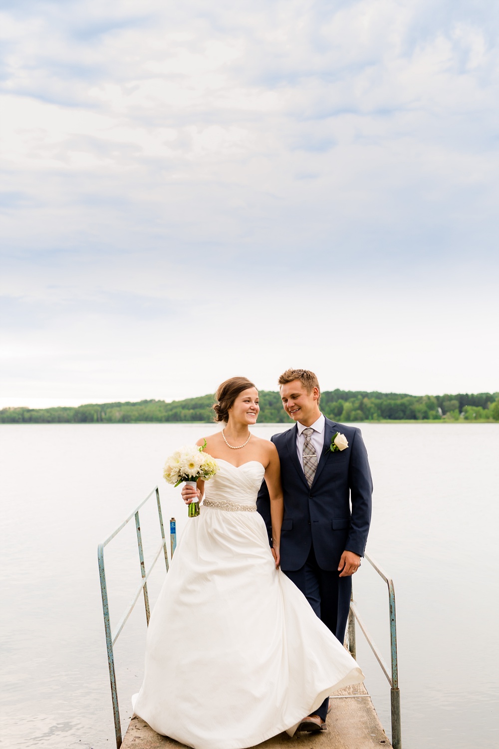 Wolf Lake, MN Country Styled Wedding, White Dress, Blue Suite | Photographed by Amber Langerud Photography | Bride &amp; Groom Walking on a Dock