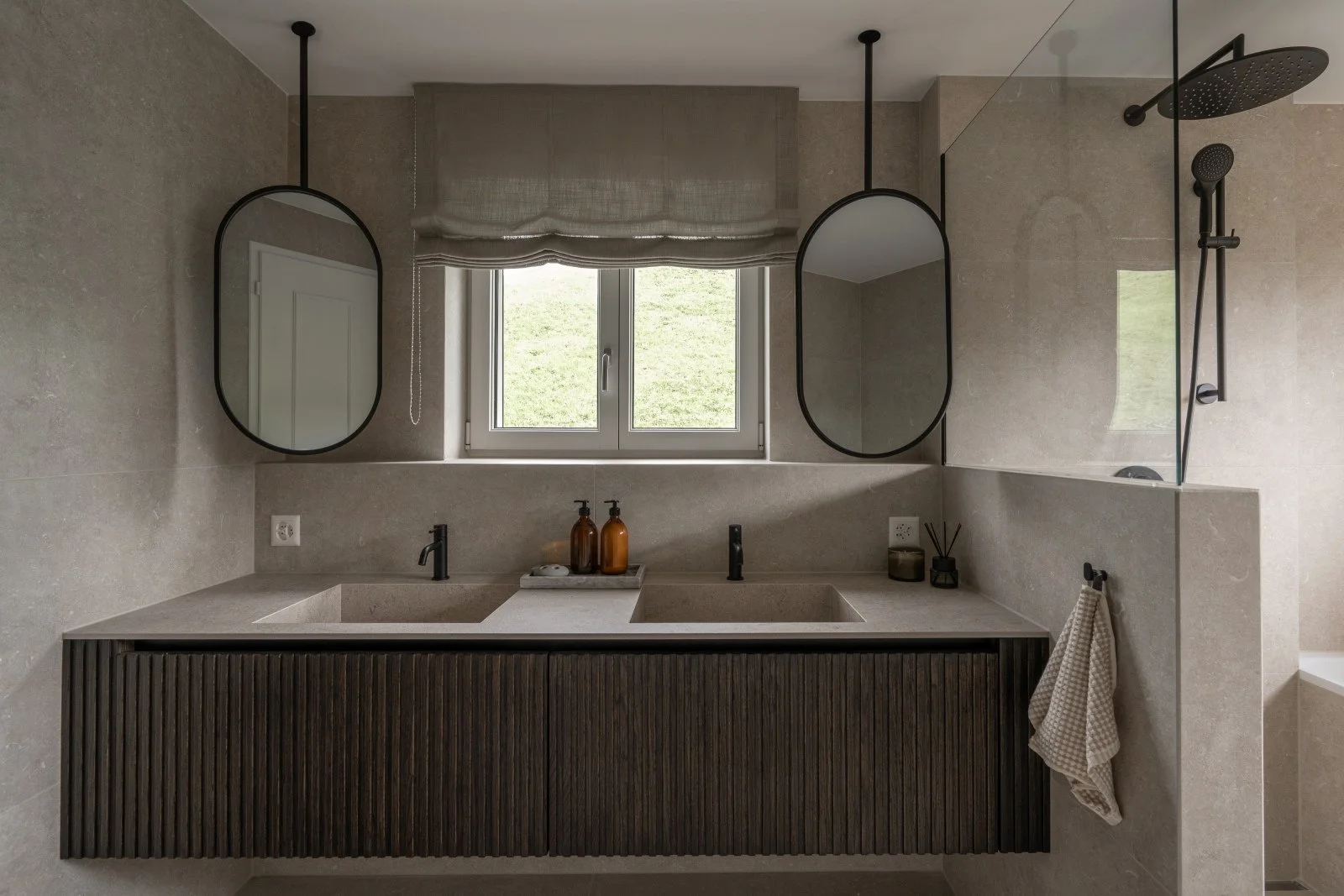 Main bathroom with double stone vanity, dark wood cabinetry and suspended mirrors at Landhaus Ennetmoos.