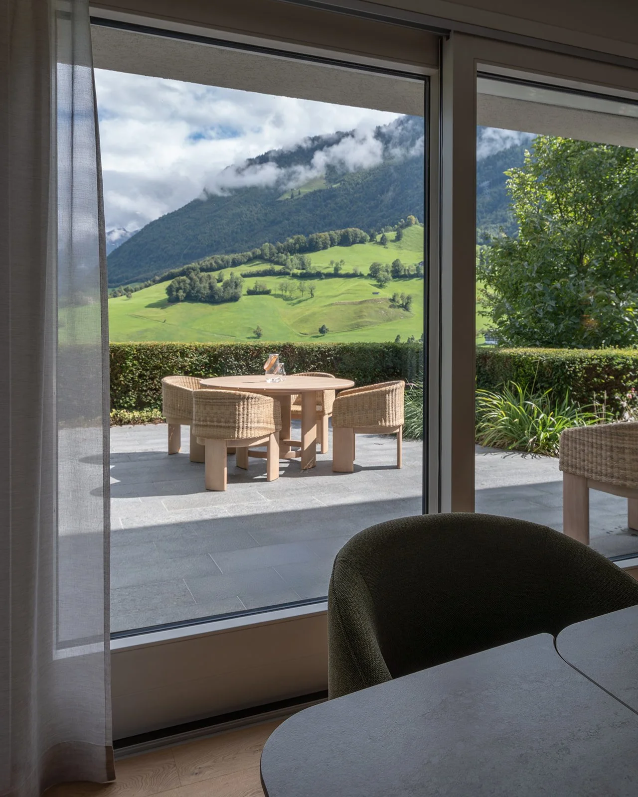 View from the interior towards the outdoor dining terrace and mountain landscape at Landhaus Ennetmoos.