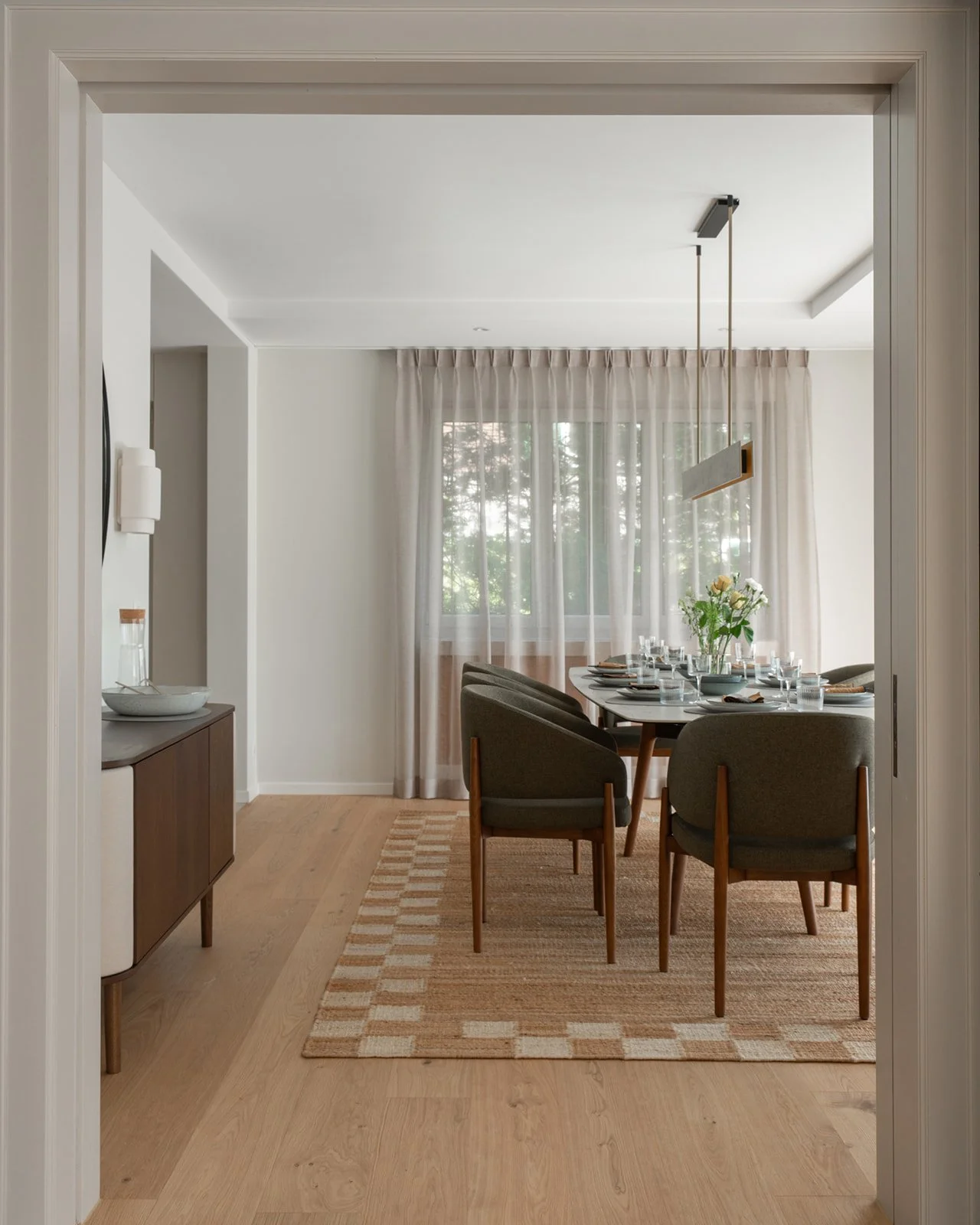 View into the dining room with upholstered chairs, patterned rug and linear pendant light.