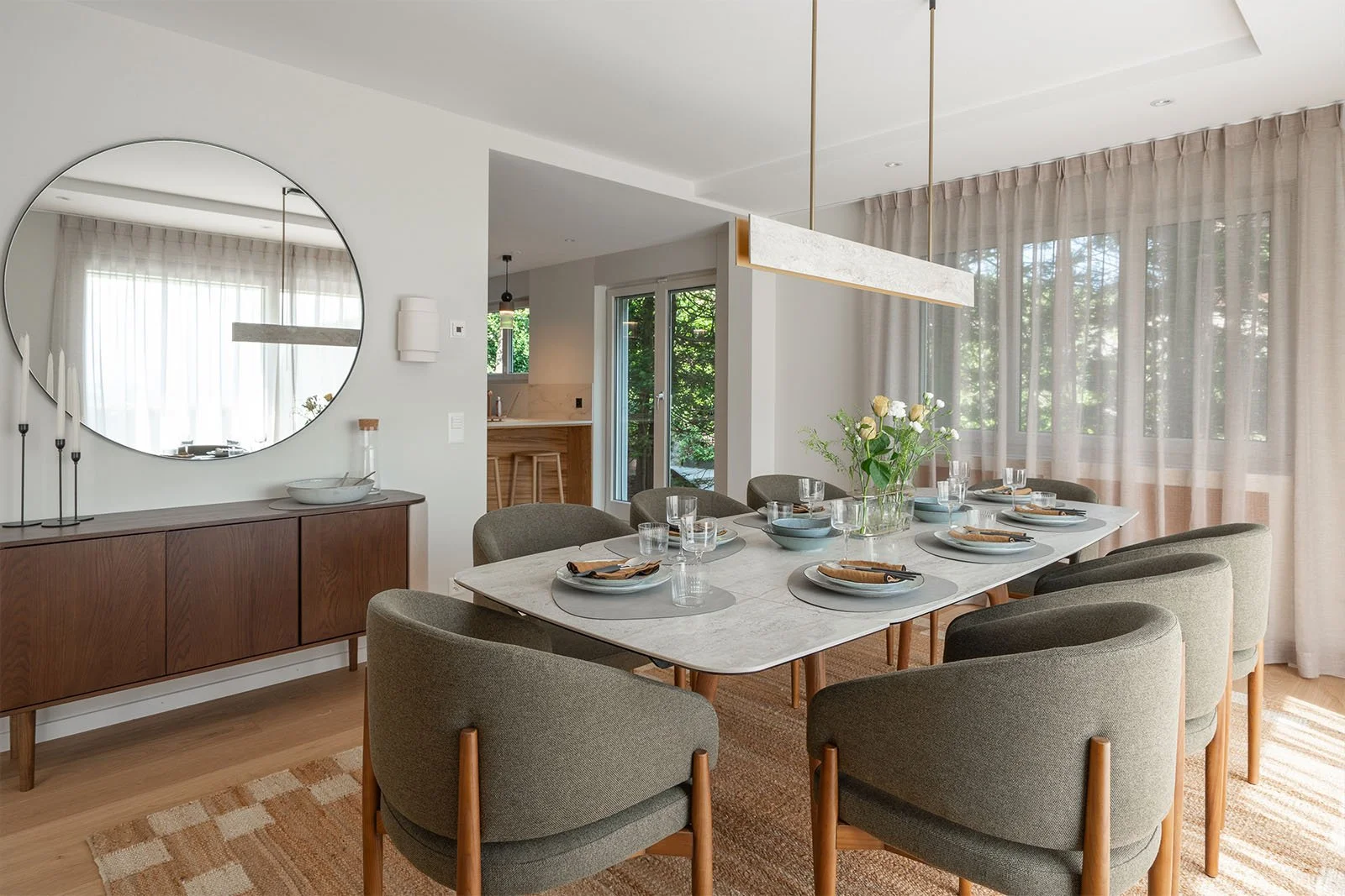 Dining room with an extendable dining table seating up to eight, upholstered chairs and a large round mirror.