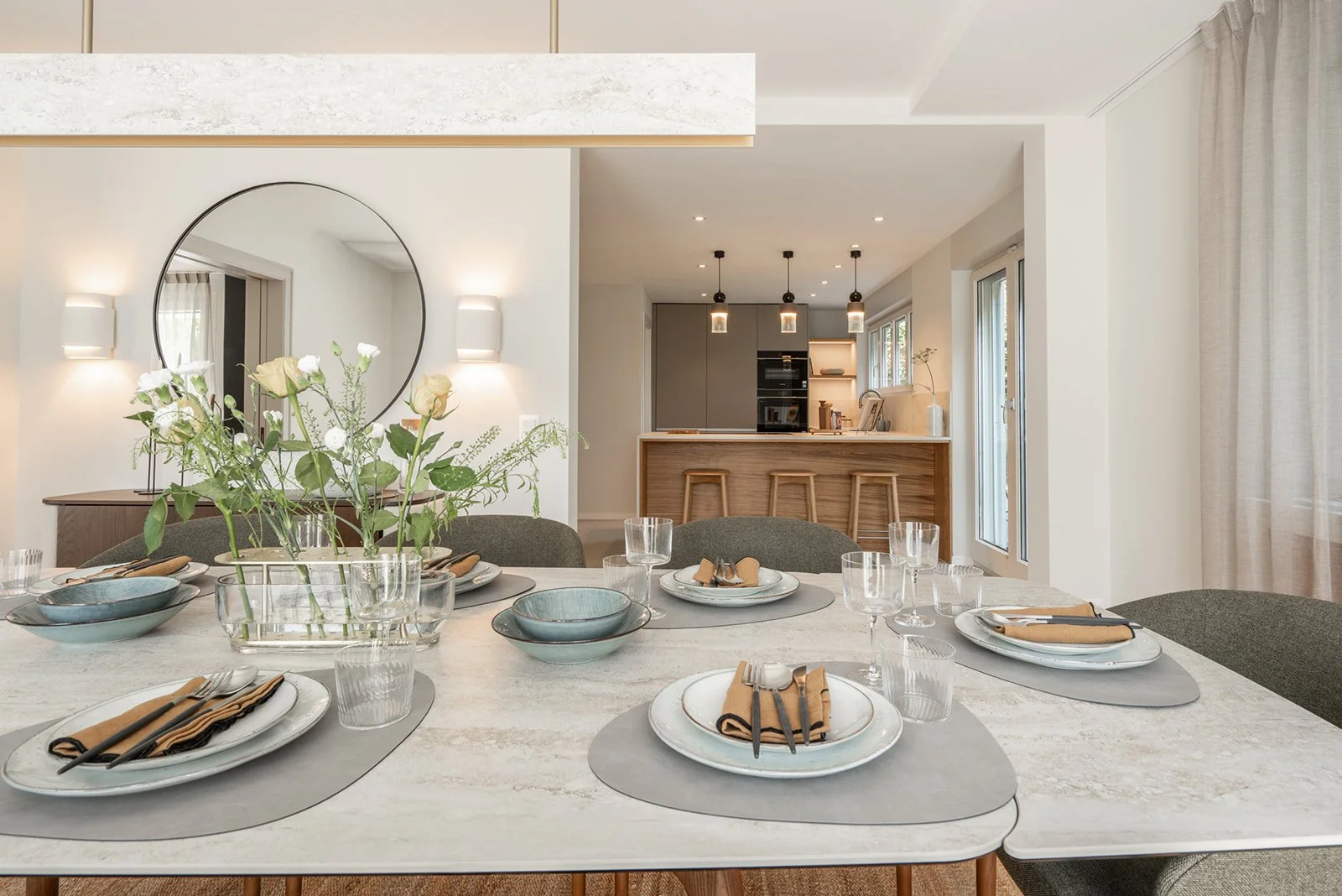 Set dining table with floral arrangement and view towards the adjoining kitchen at Landhaus Ennetmoos.