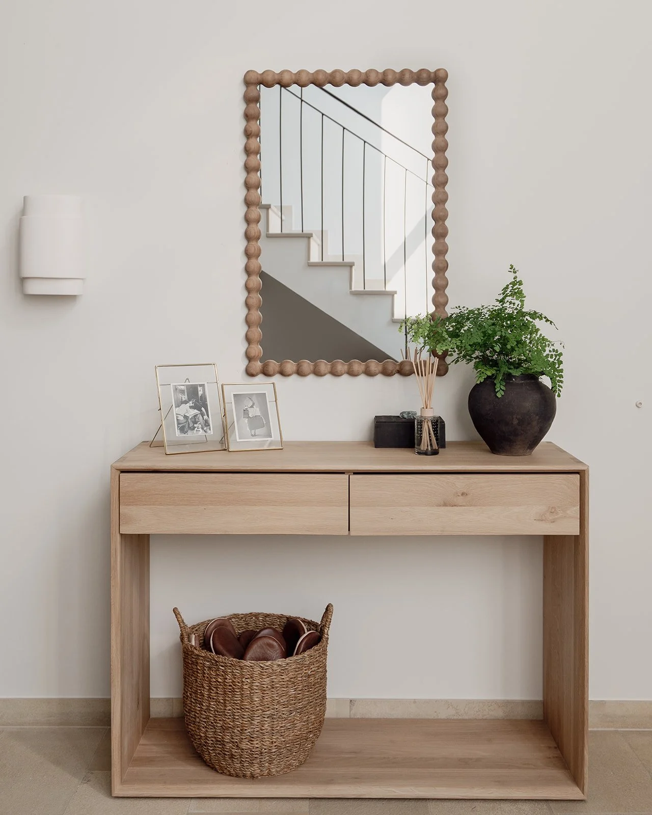 Oak console in the entrance hall styled with framed photographs, greenery and a sculptural wooden mirror.