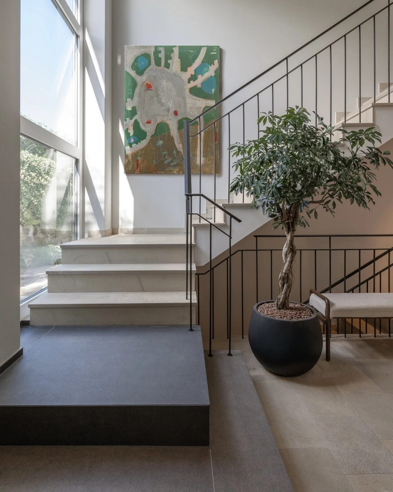 Entrance staircase with two contrasting lower steps designed as an architectural accent, black metal railings, large artwork and indoor tree.
