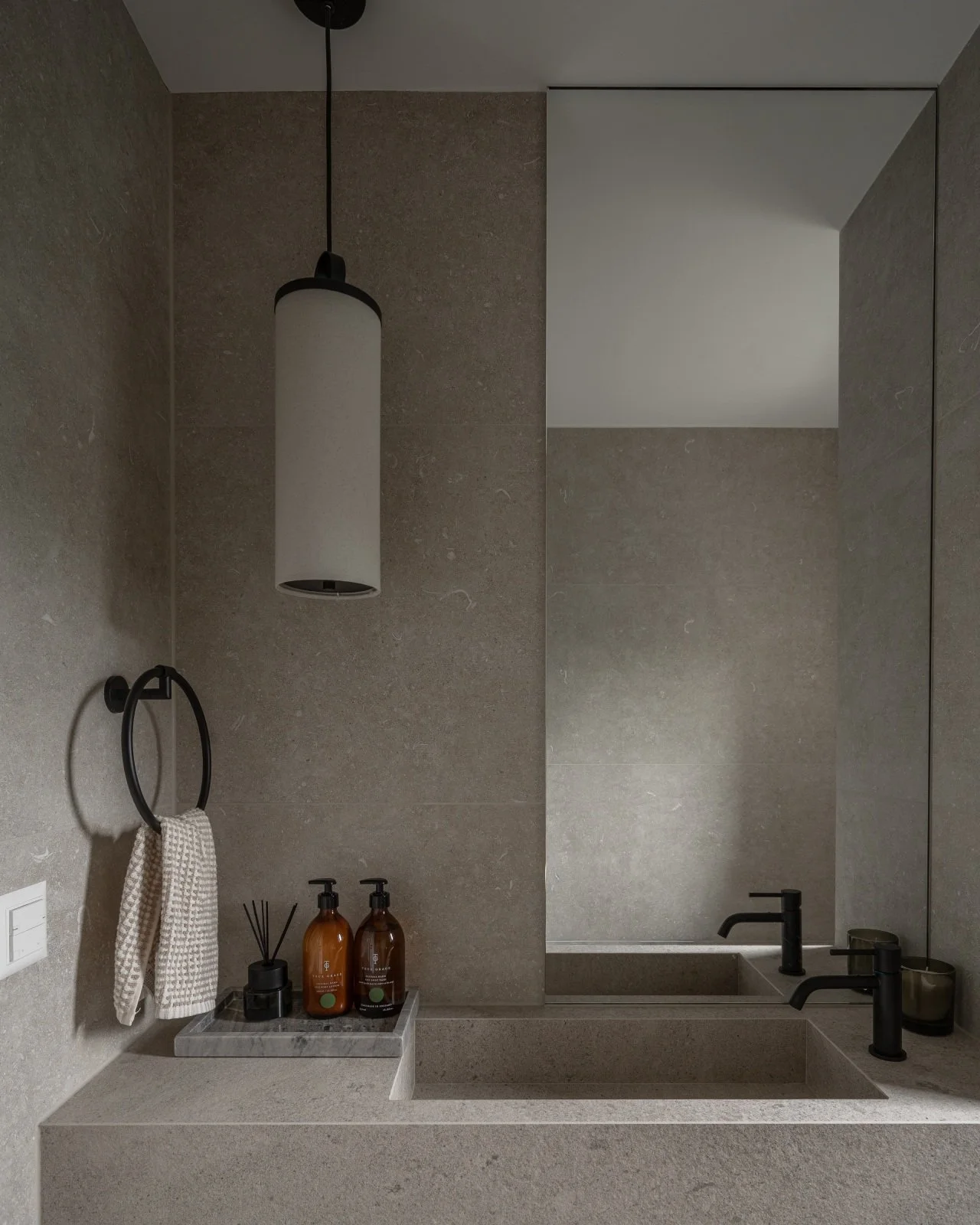 Bathroom vanity with integrated stone basin, pendant light and full-height mirror.