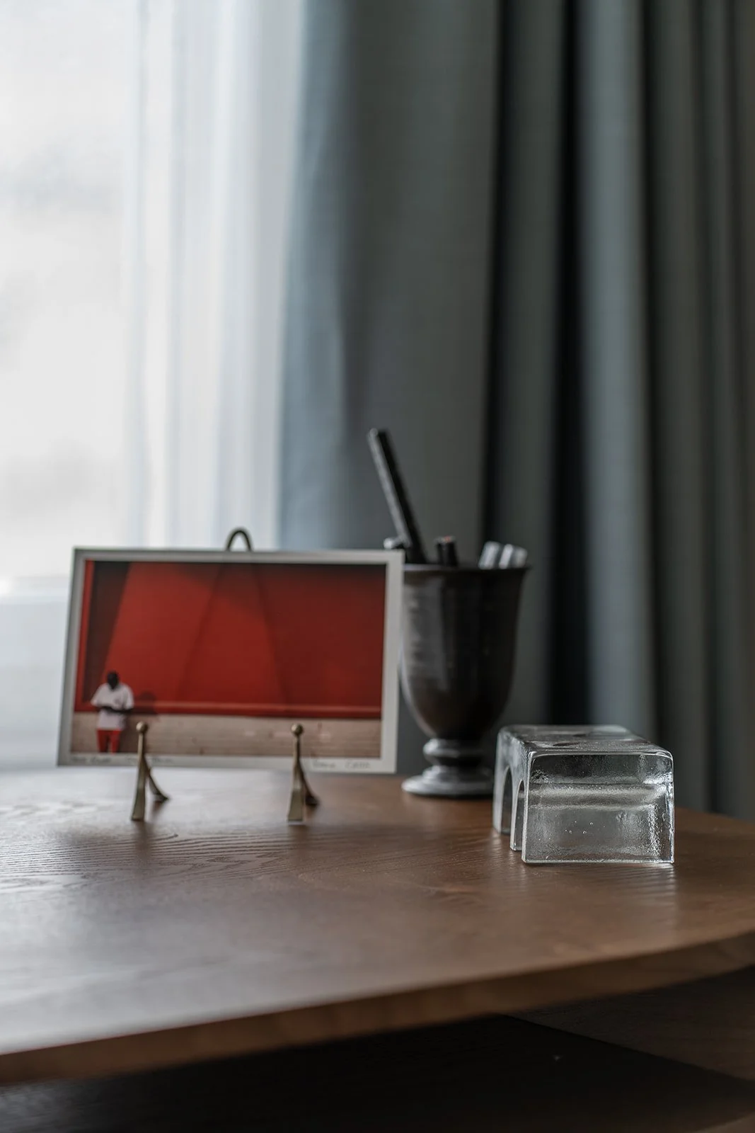 Detail of the home office desk with curated objects and a framed photograph, set against soft blue-grey curtains.