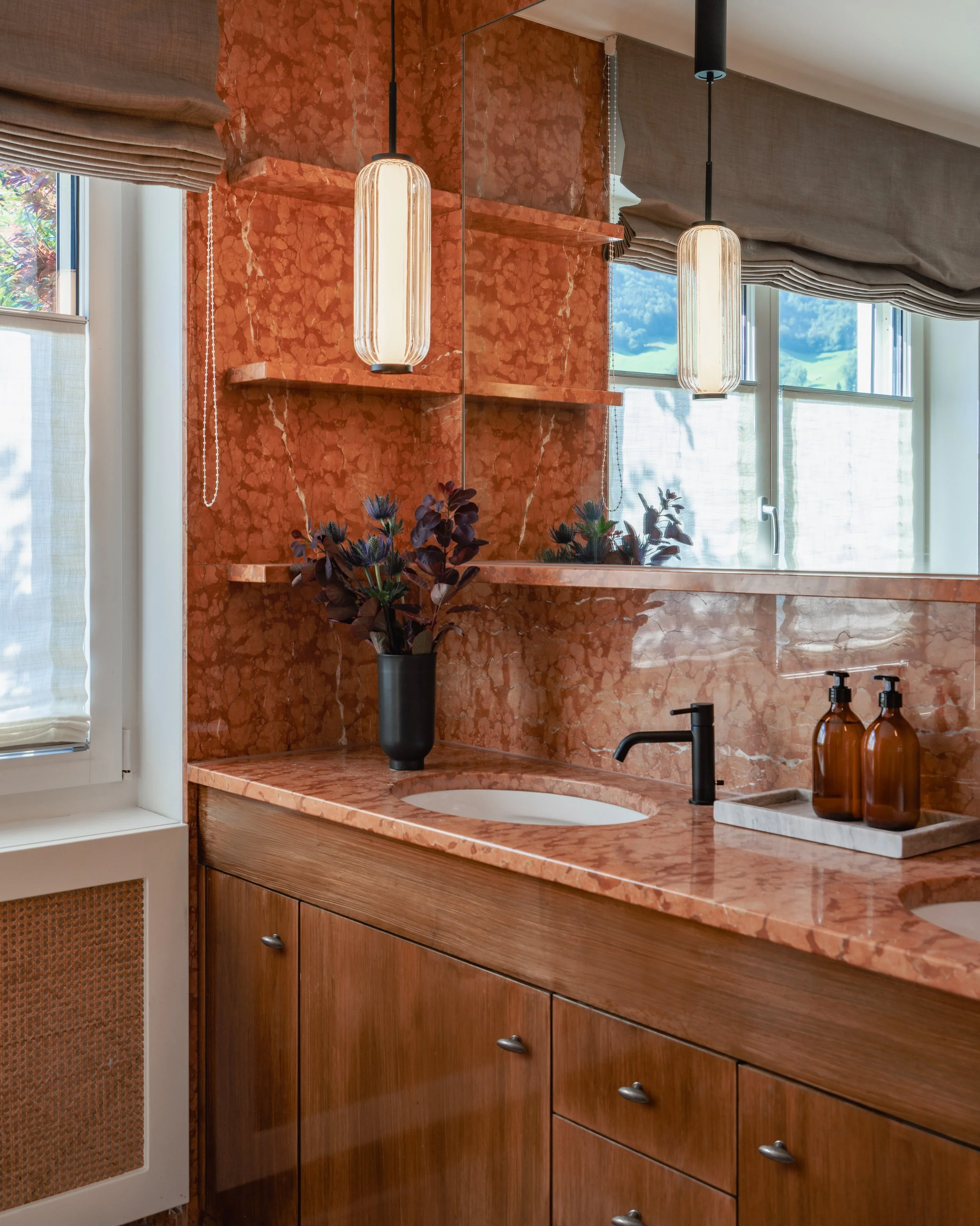 Detail of the master bathroom vanity combining richly veined red marble, warm wood cabinetry, black fittings and ribbed glass pendant lighting.