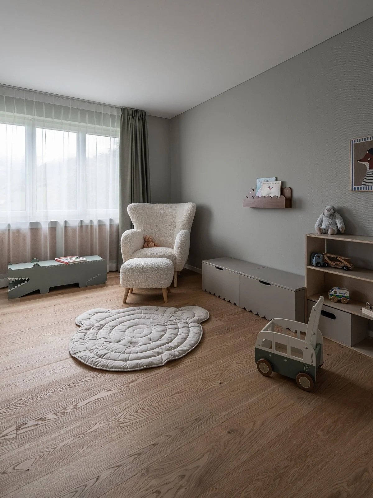 Calm kids’ room with wooden flooring, soft neutral furnishings, toy storage and a reading chair at Landhaus Ennetmoos.
