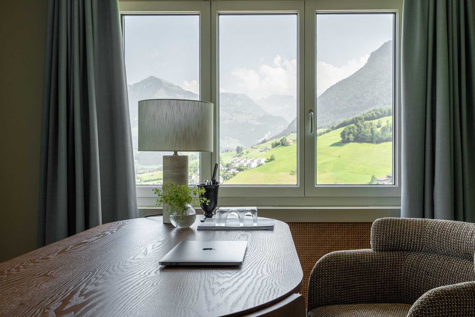 Guest room and home office overlooking the surrounding mountains, with a sculptural wooden desk positioned to make the landscape part of the working environment.