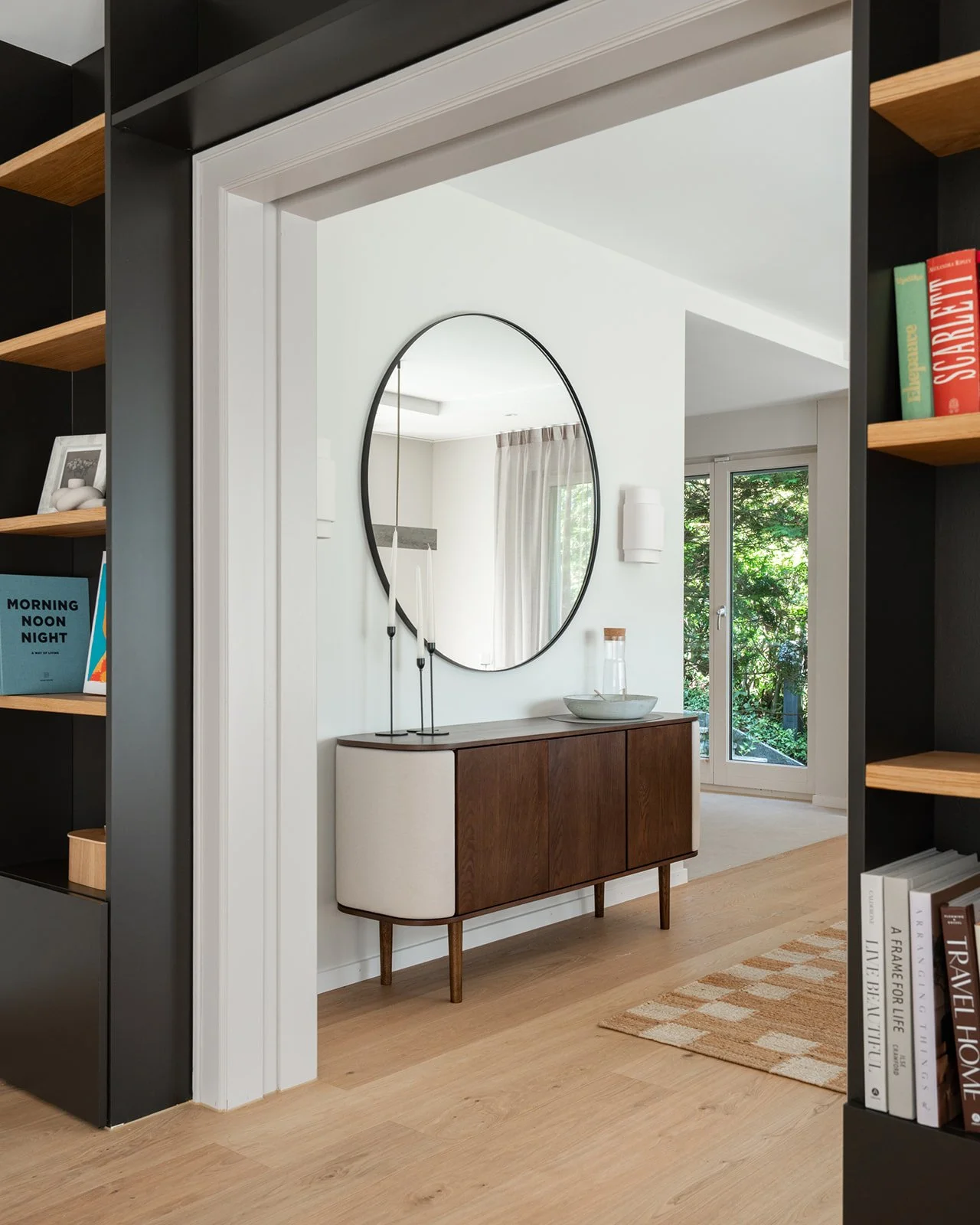Dining room sideboard and round mirror framed by the dark built-in shelving at Landhaus Ennetmoos.