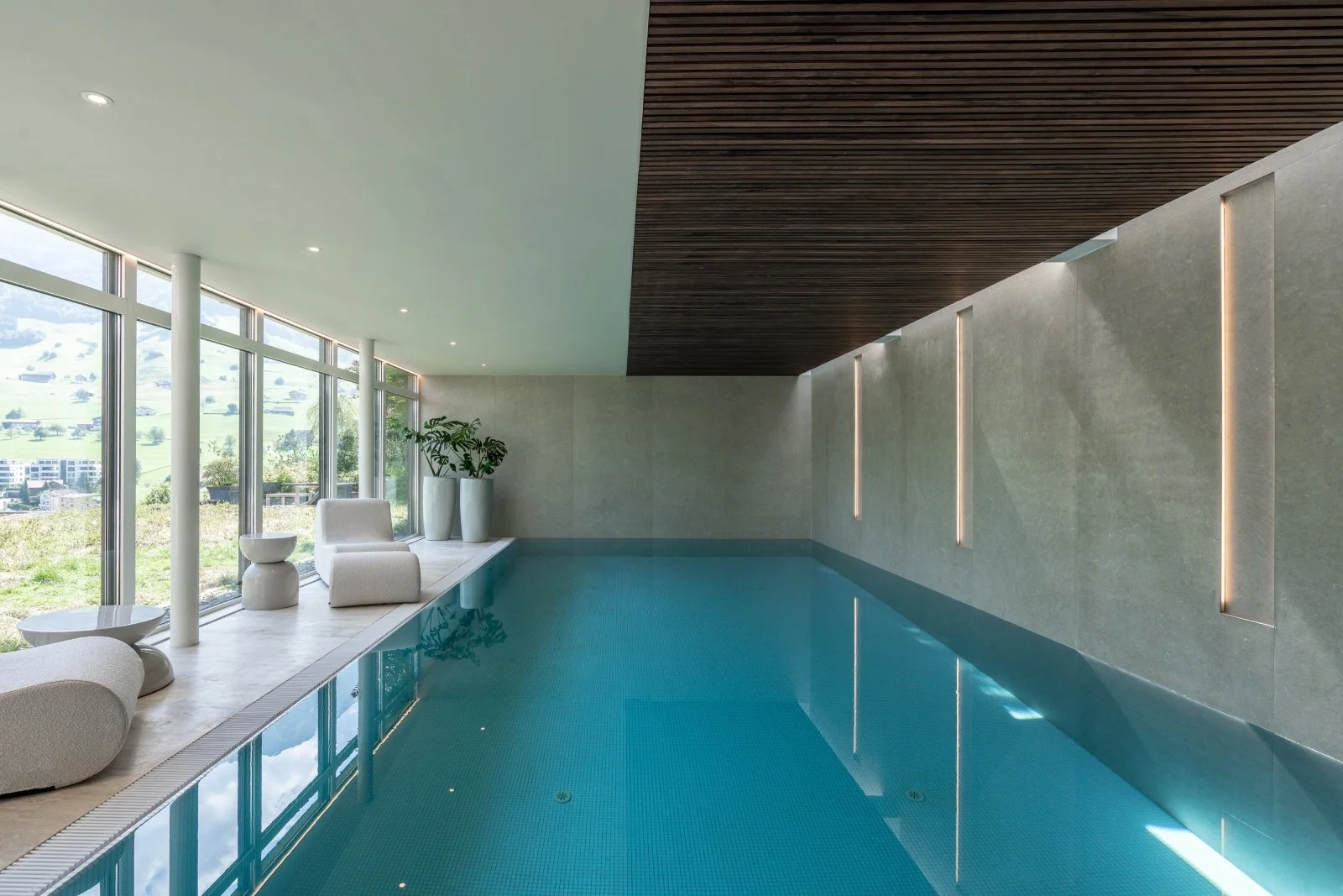 Indoor swimming pool with timber ceiling, integrated wall lighting and floor-to-ceiling glazing.