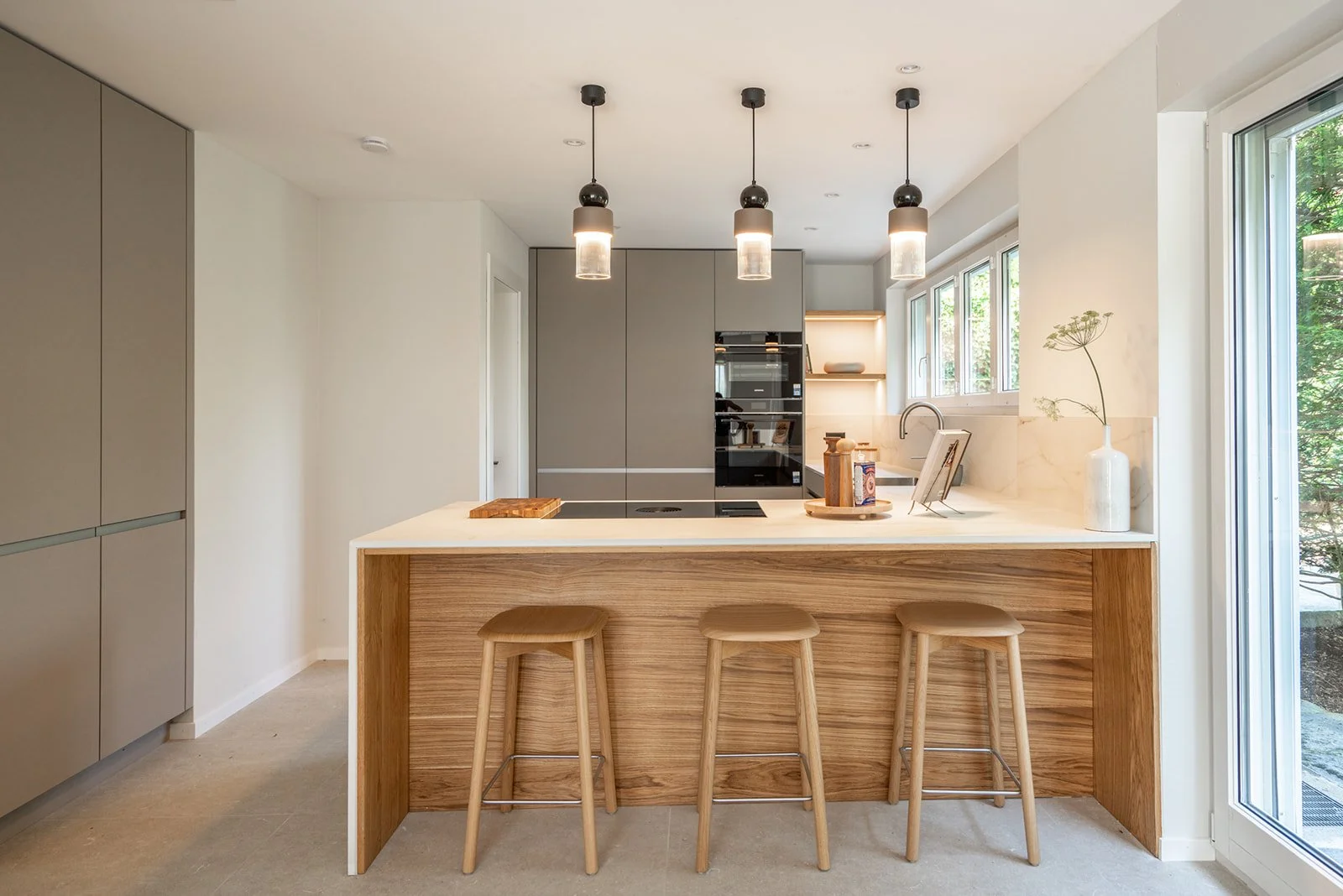 Contemporary kitchen with a warm oak island, stone worktop, wooden bar stools and three pendant lights.