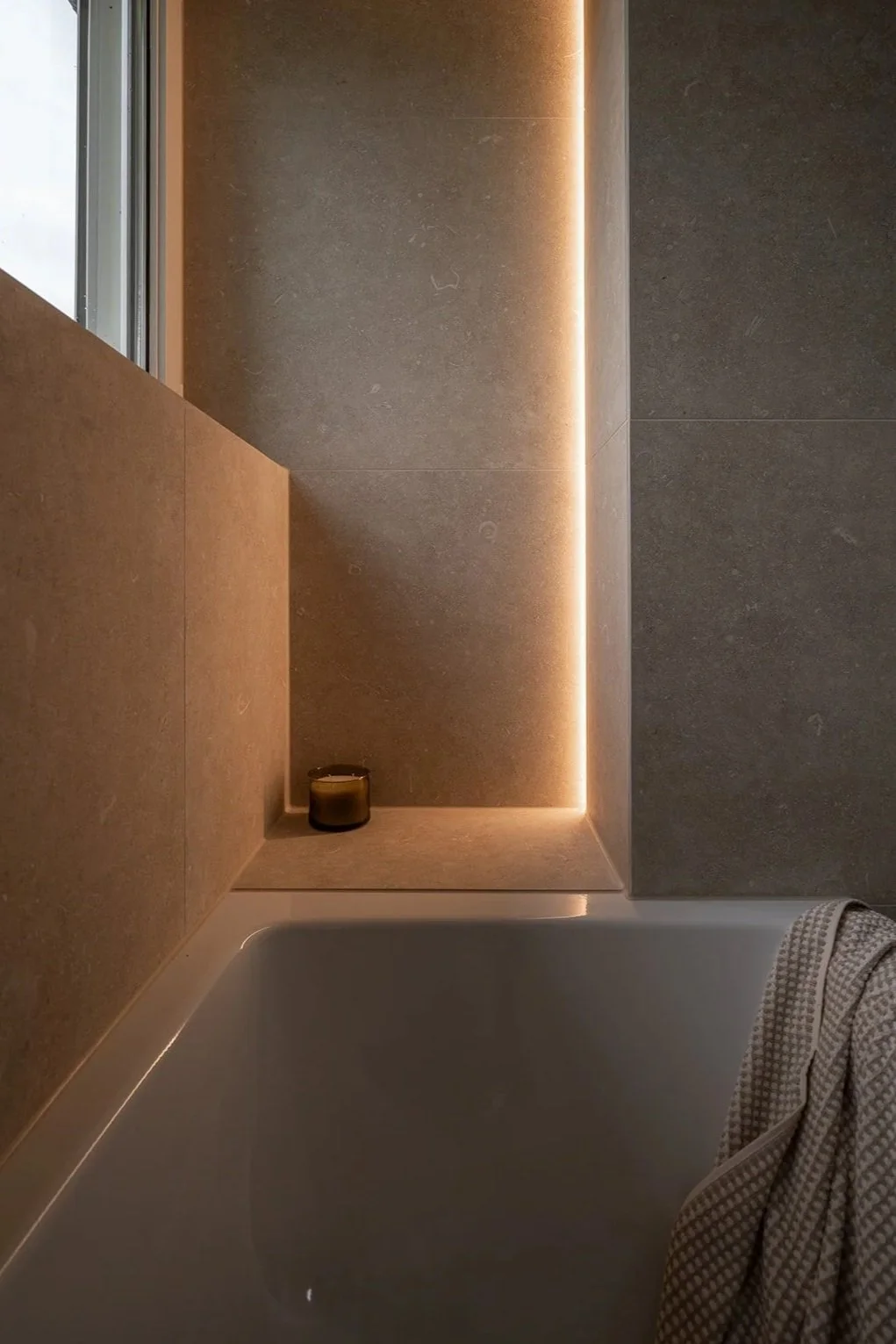 Bathtub corner with integrated warm lighting and large-format stone tiles.