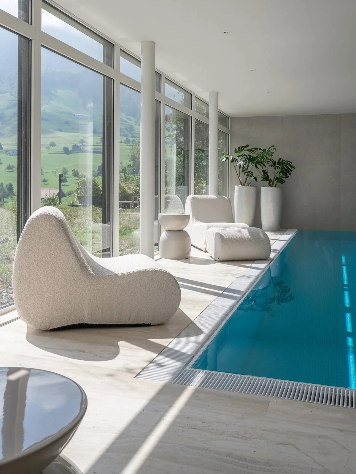 Indoor pool lounge with sculptural white seating and panoramic views of the Swiss landscape.