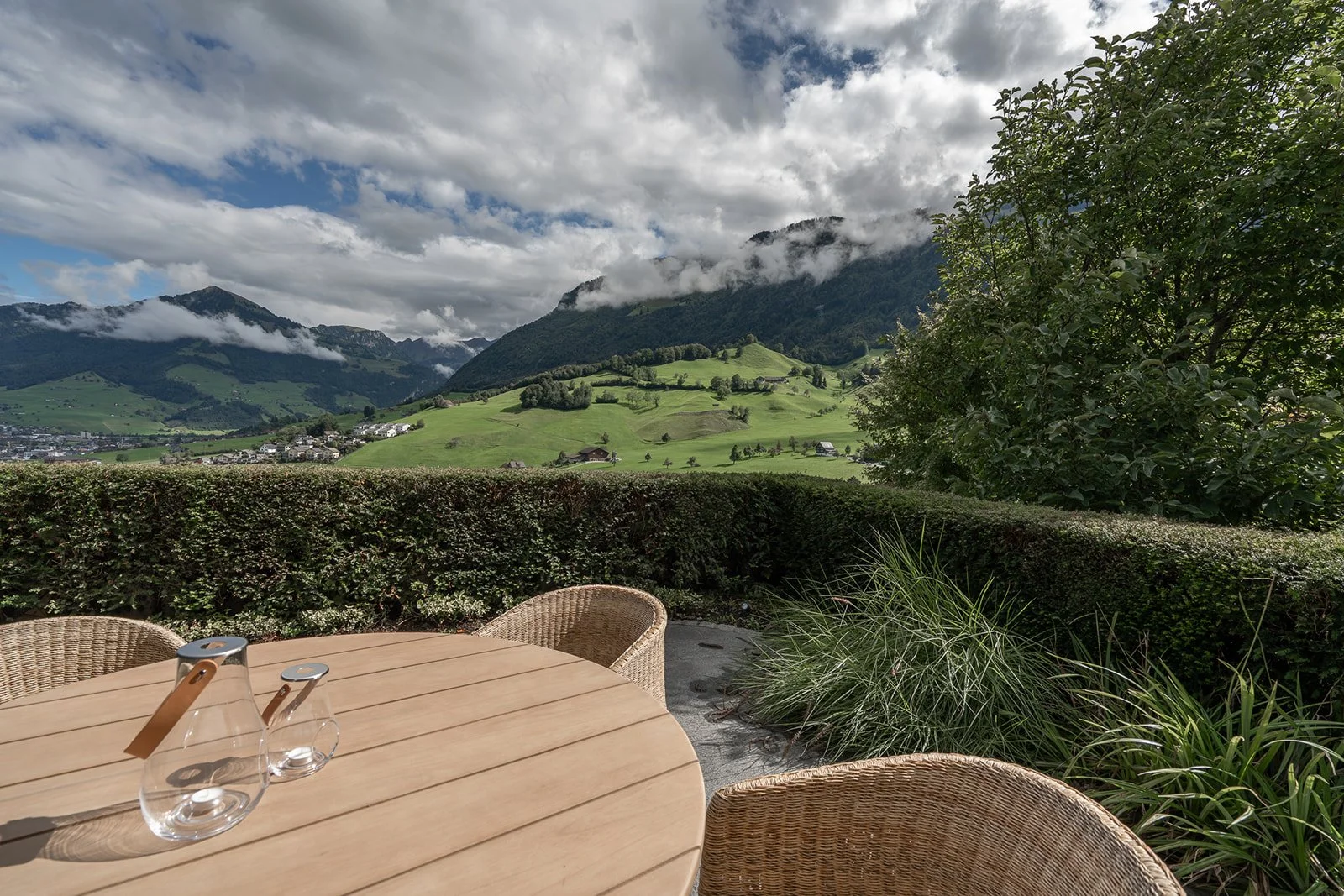 Outdoor dining area with timber table and woven chairs overlooking the mountain landscape at Landhaus Ennetmoos.