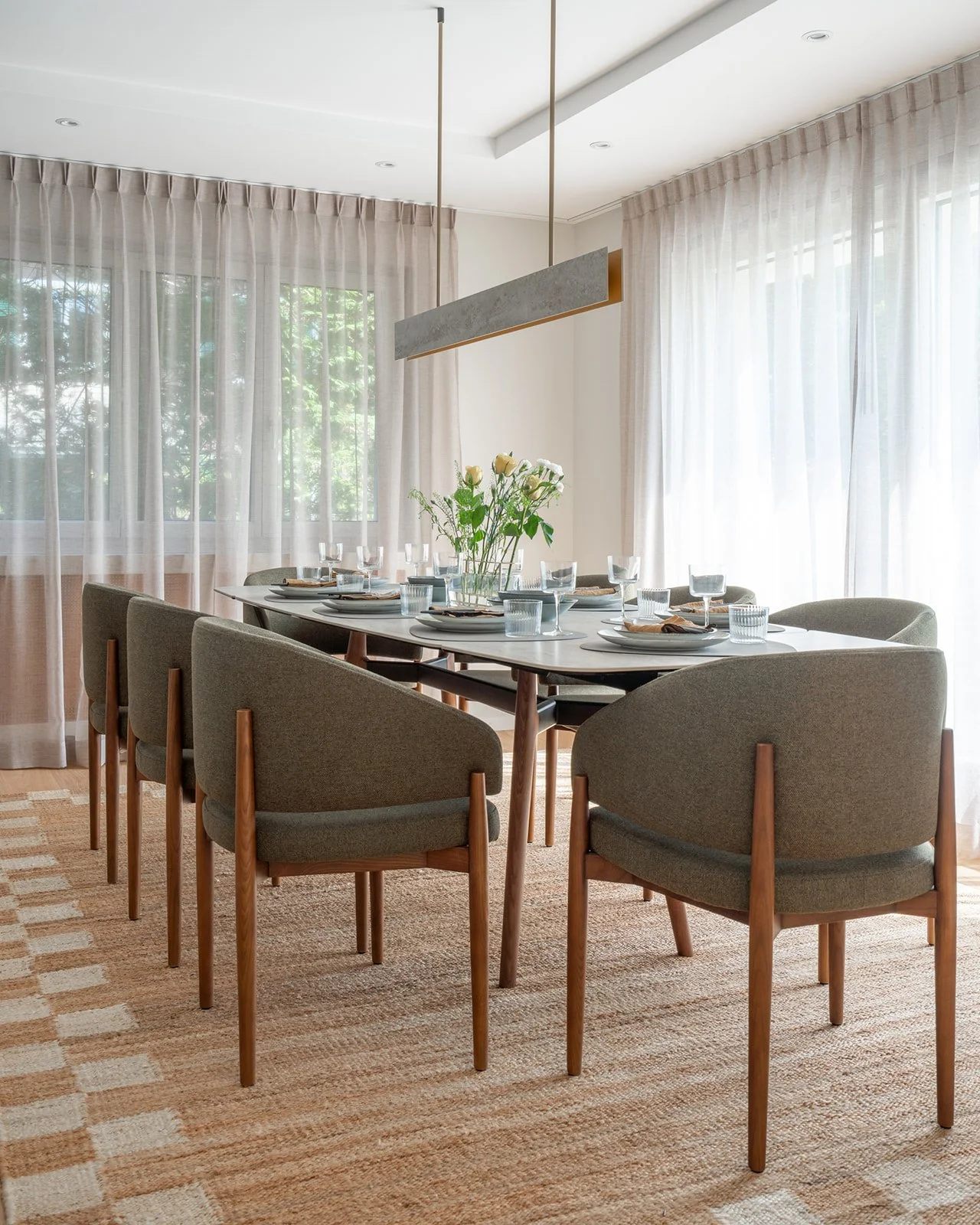 Dining room with upholstered chairs, textured rug and sculptural linear pendant above the table.