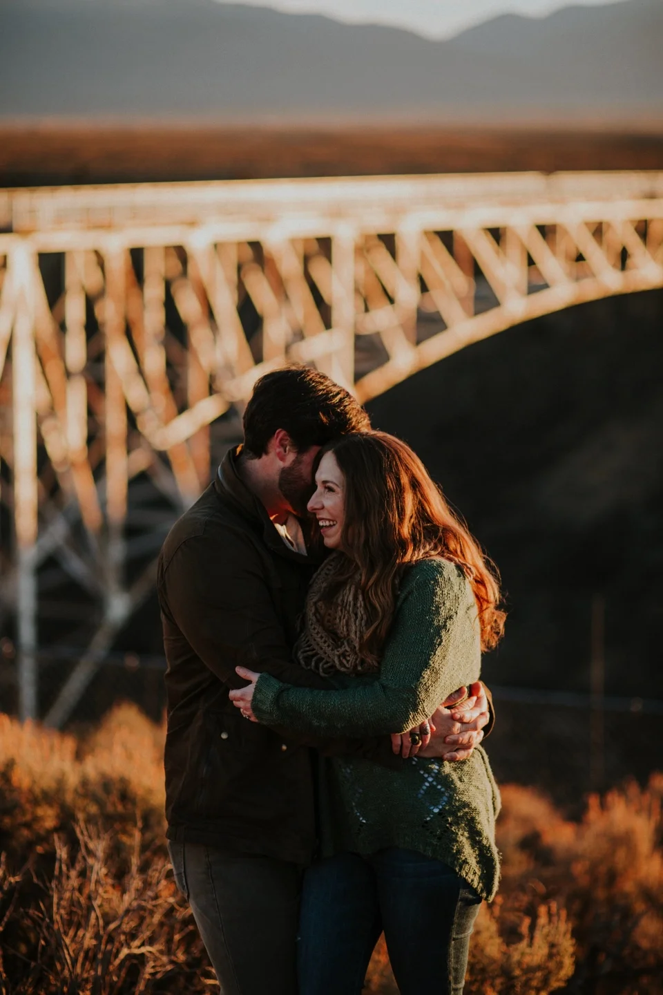 Natalie and Boots traveled all the way from the sunshine state for their beautiful Sunrise Engagement Photos at the Rio Grande Gorge Bridge in Taos, New Mexico. It was a chilly morning in Taos and we were all pretty frozen! It was 6 degree weather when we met at the Rio Grande Gorge Bridge, but there is nothing in the world like seeing the sun rise at the gorge bridge in Taos. The golden light and cotton candy skies from the sunrise were absolutely gorgeous! Natalie and Boots had the perfect winter engagement outfit inspiration for these chilly sunrise engagement photos.